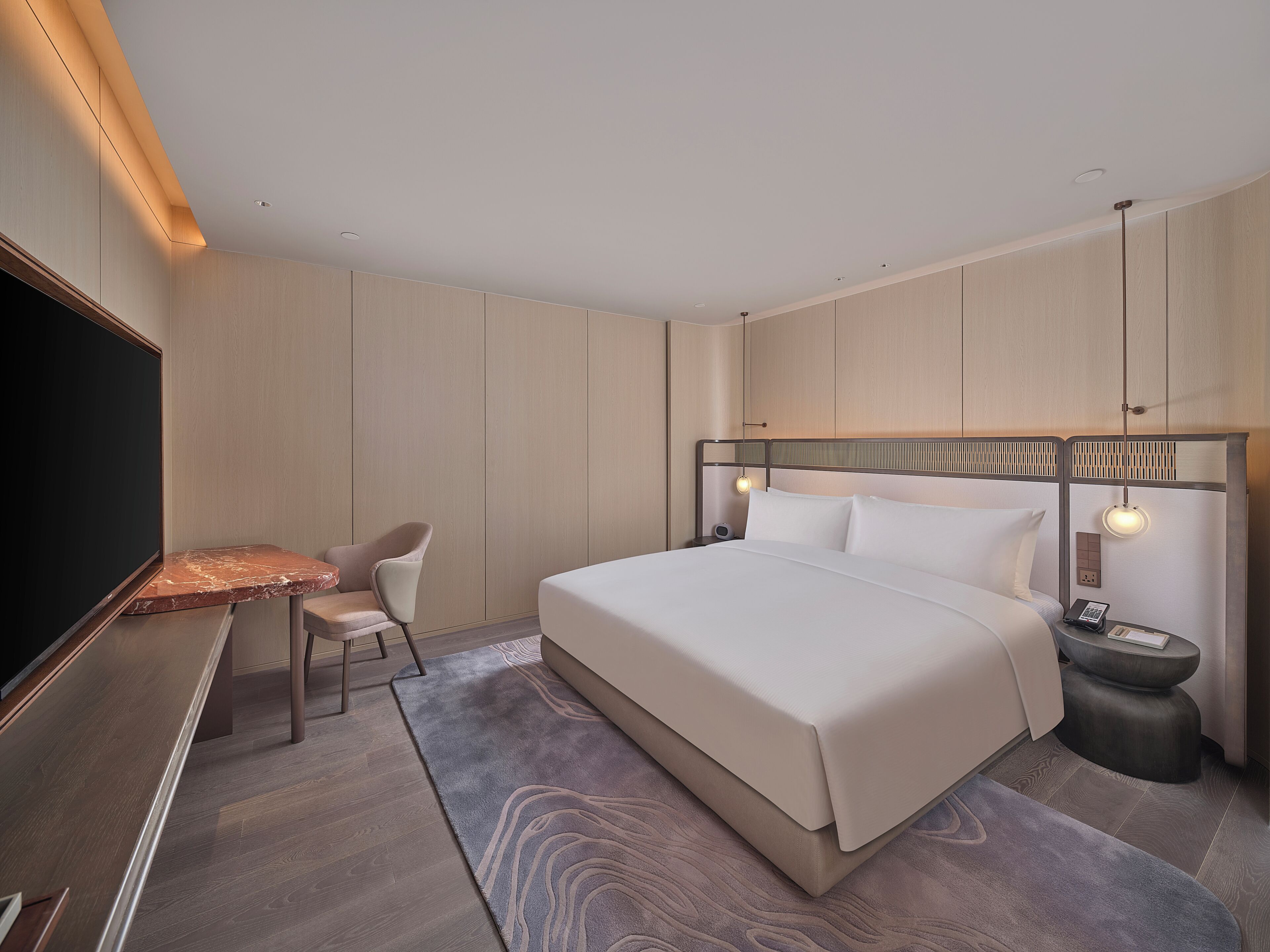 A hotel room with a bed, bedside table, chair, TV, and a desk.