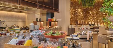A buffet with various food items and beverages, a wooden cabinet, and a decorative wall with hanging plants.