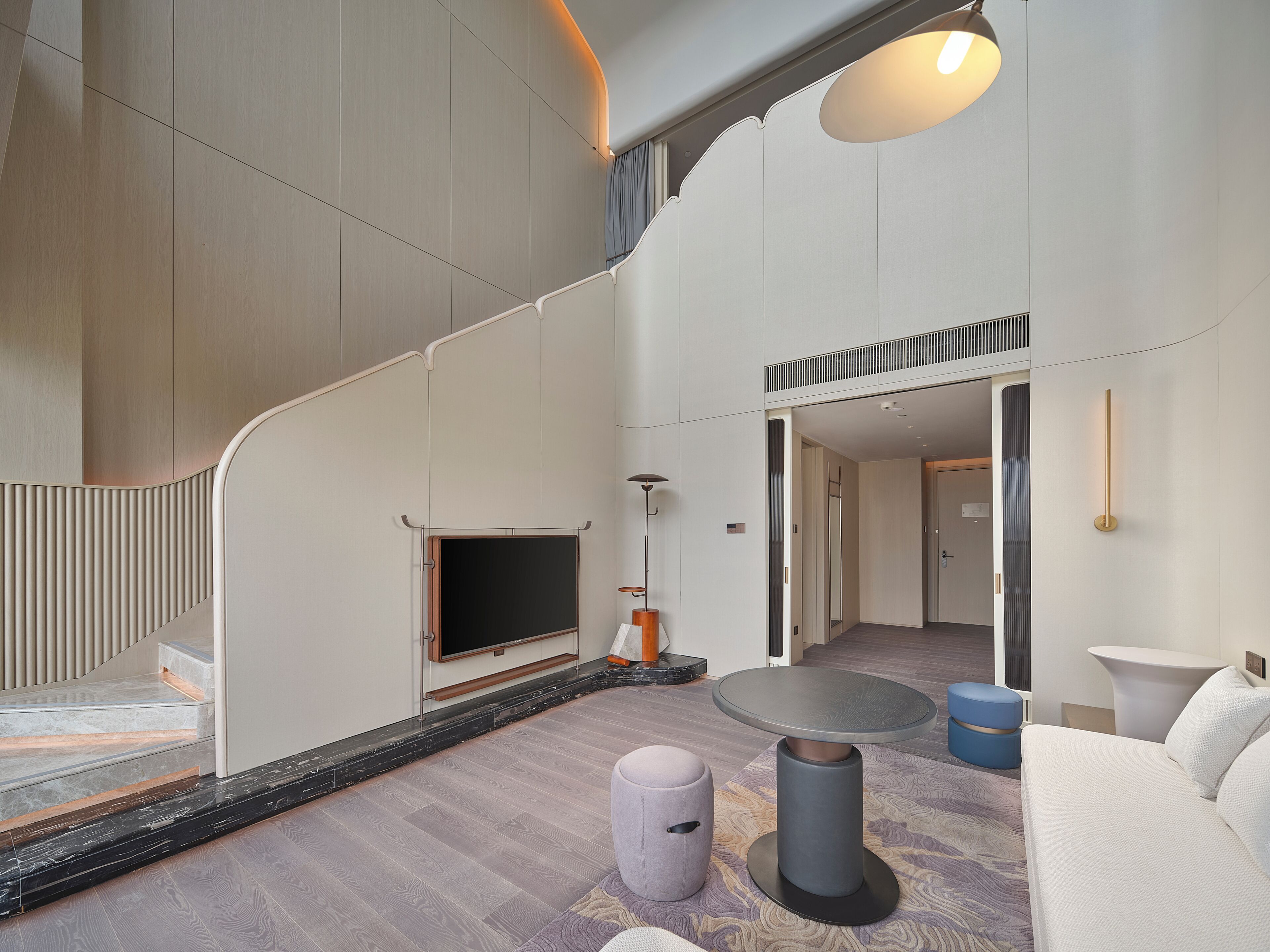 A modern interior with a staircase, a flat-screen TV, a round table, and a sofa.