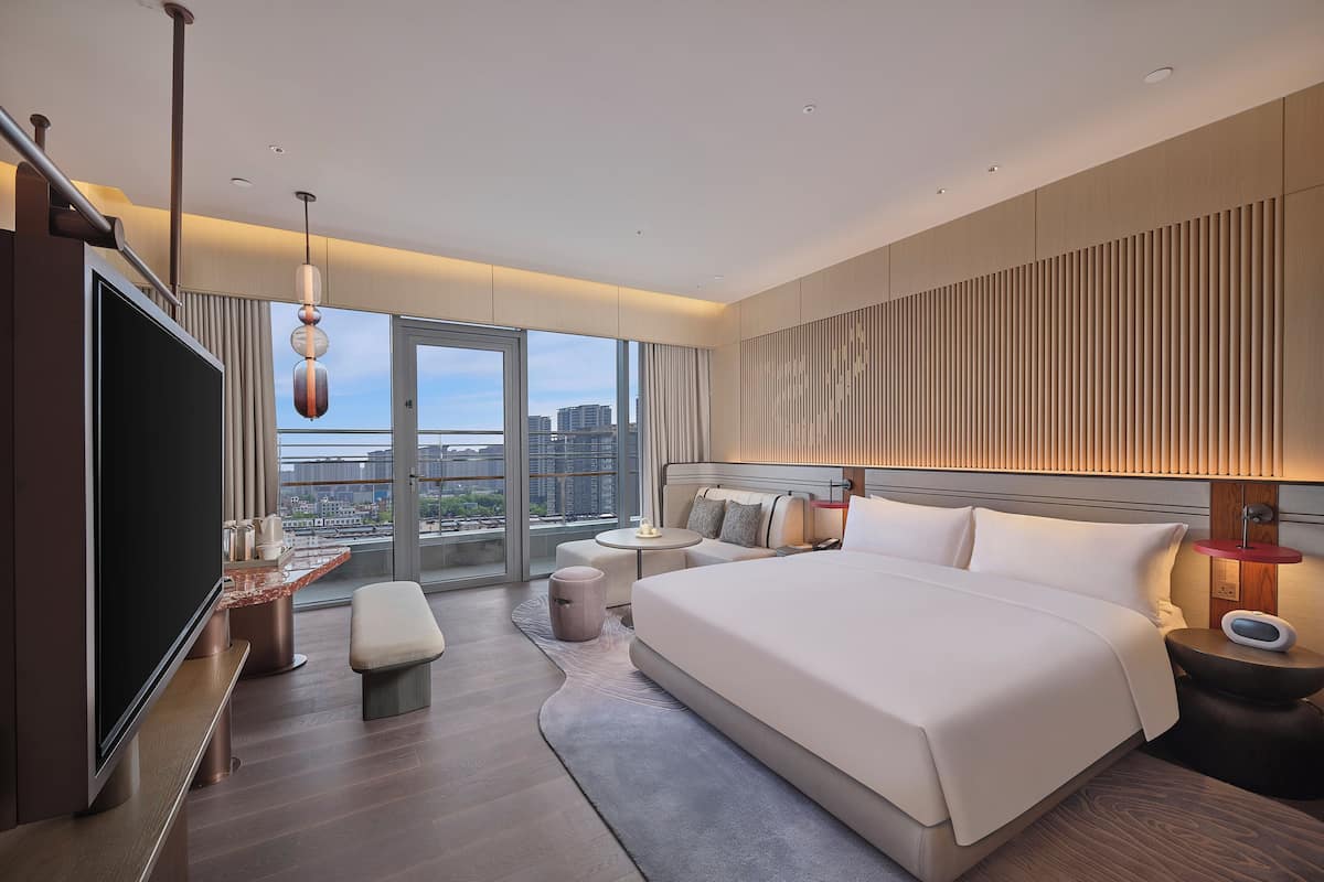 Een moderne hotelkamer met een groot bed, een flatscreen televisie, een zithoek en uitzicht op de stad.