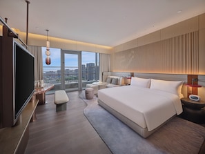 Une chambre dâhĂŽtel moderne dotĂ©e dâun grand lit, dâune tĂ©lĂ©vision Ă Ă©cran plat, dâun coin salon et offrant une vue sur la ville.
