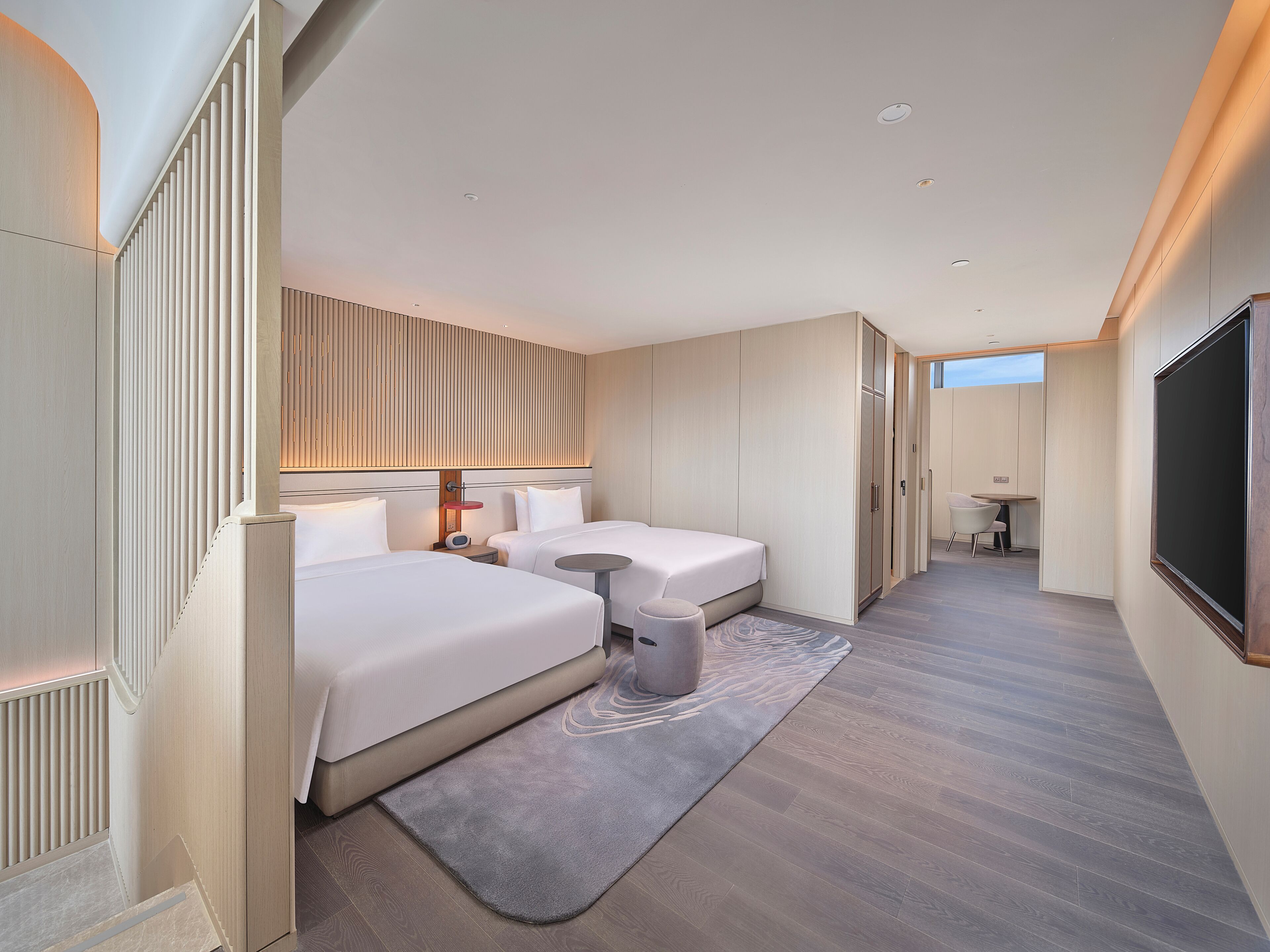 Une chambre d’hôtel moderne avec deux lits, une petite table, une chaise, un téléviseur et une grande fenêtre.
