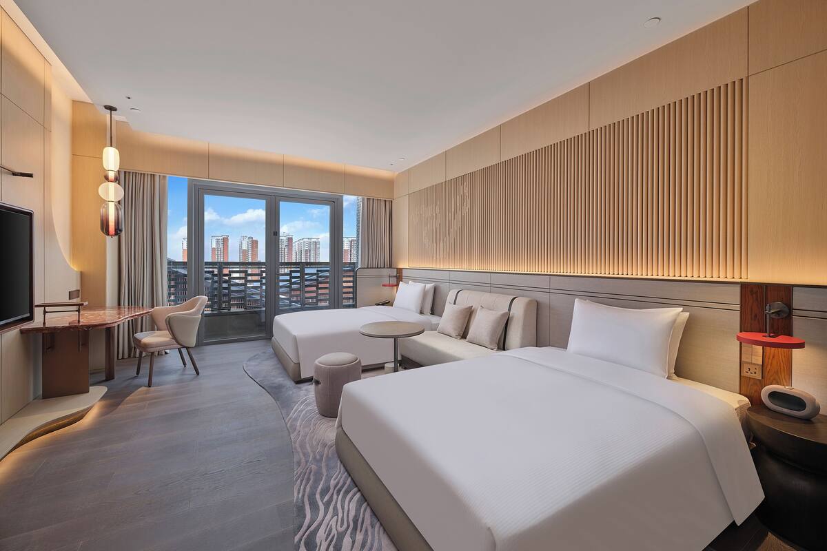 Een moderne hotelkamer met een groot bed, een bureau en uitzicht op de skyline.