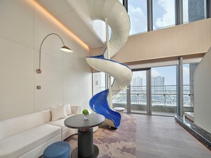 Un intĂ©rieur moderne avec un canapĂ© blanc, une table ronde ornĂ©e dâun vase, une chaise bleue et une structure en spirale blanche.