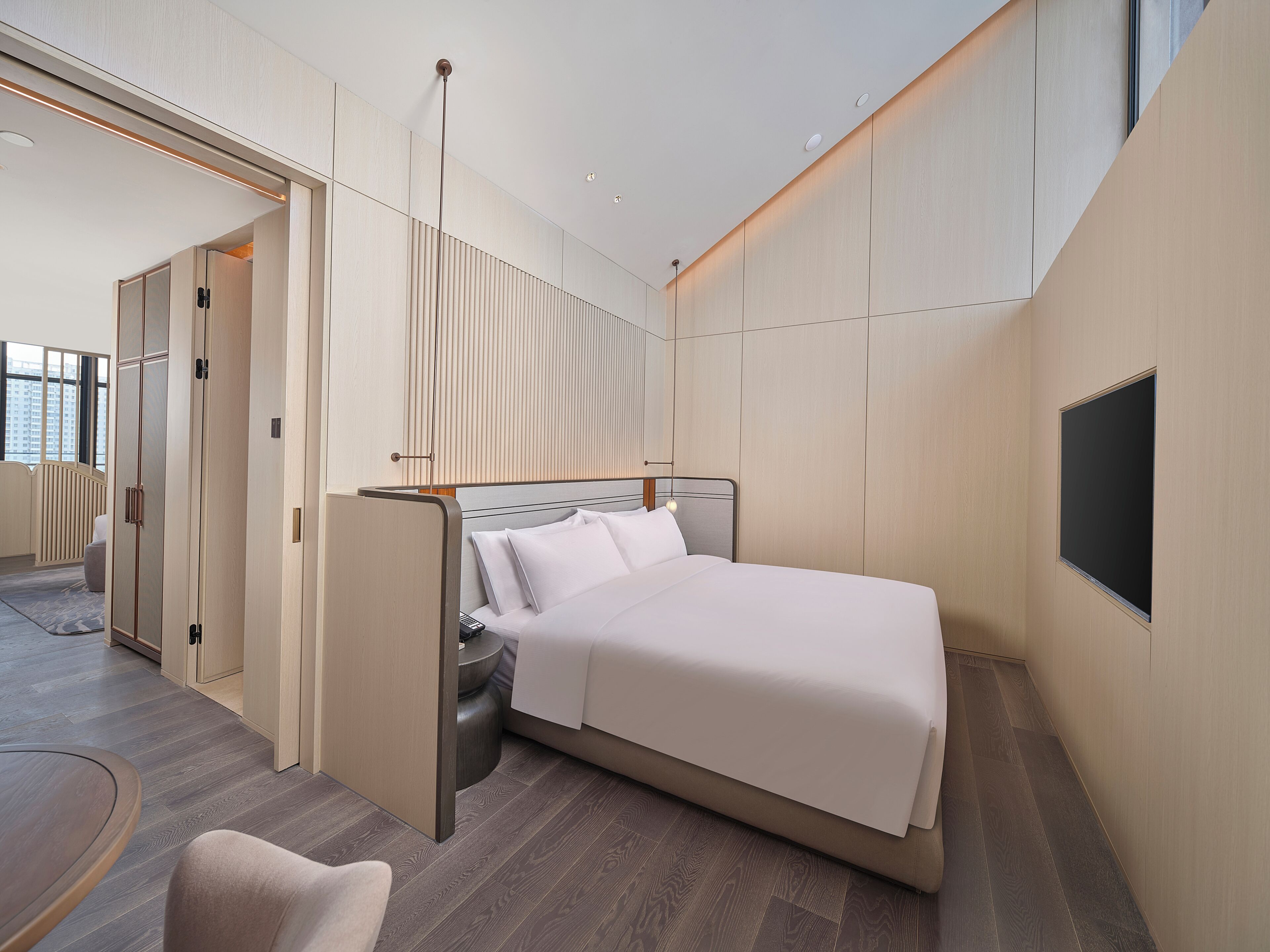 Une chambre d’hôtel moderne dotée d’un grand lit, d’un téléviseur fixé au mur et d’un coin salon séparé avec une chaise et une table.