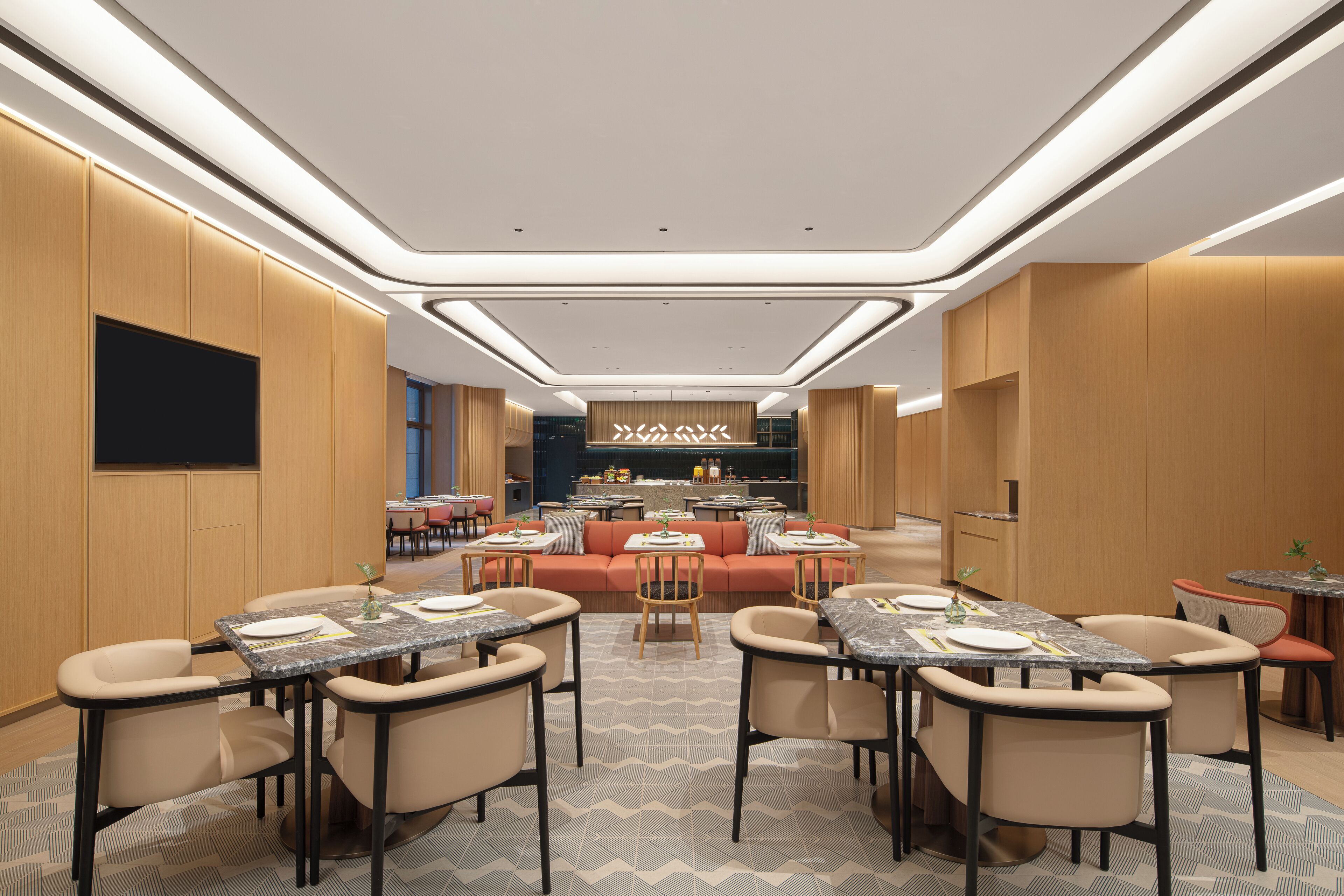 Un moderno vestíbulo de hotel con un área de estar central, varias mesas de comedor y un bar.