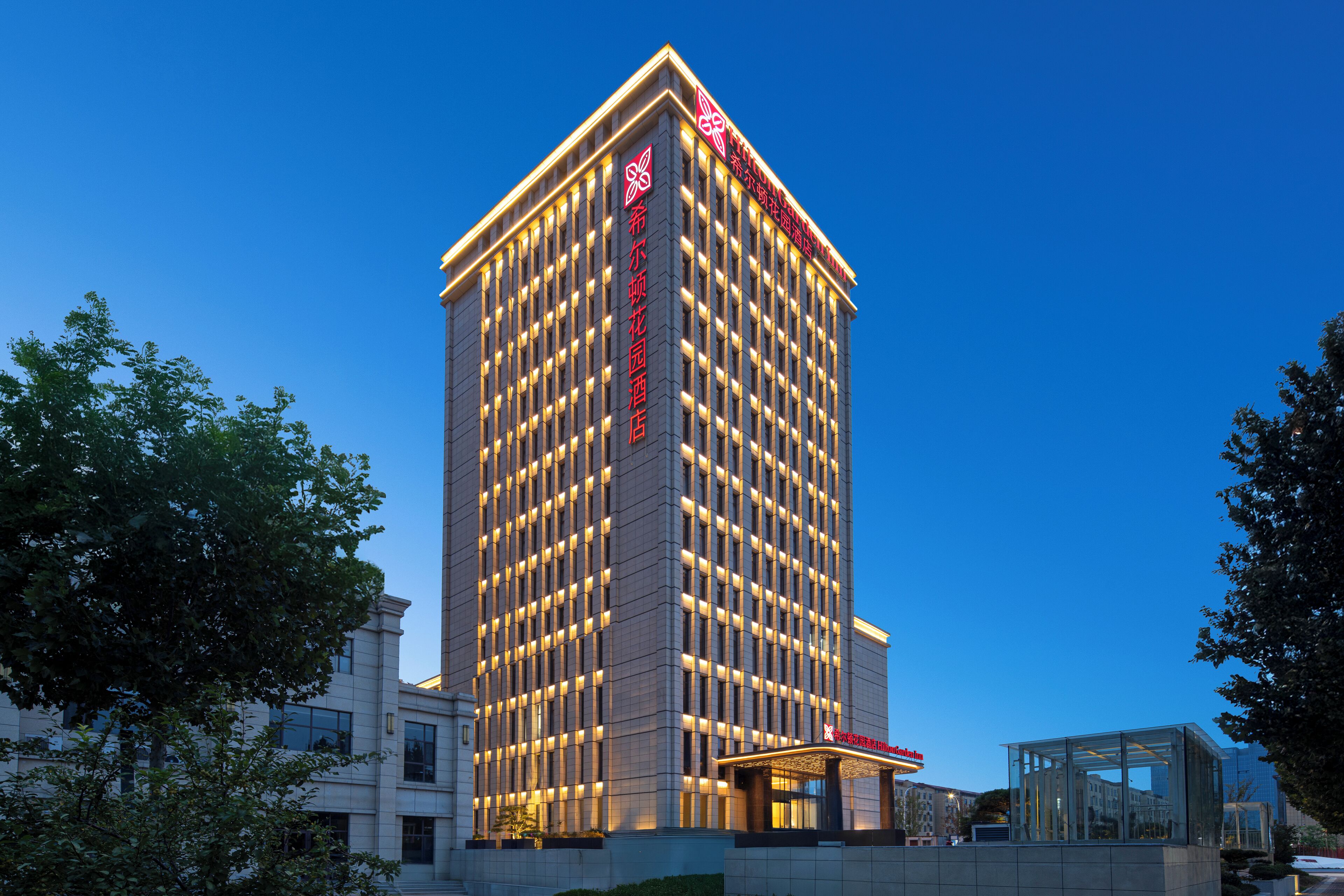Un grand immeuble d’hôtel au design moderne, doté d’une entrée imposante et d’une enseigne lumineuse.