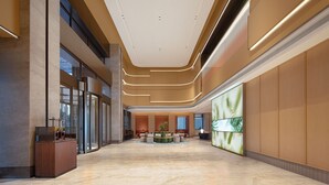 Un lobby espacioso con una zona de estar central, un mostrador de recepción y una gran pantalla digital en la pared.