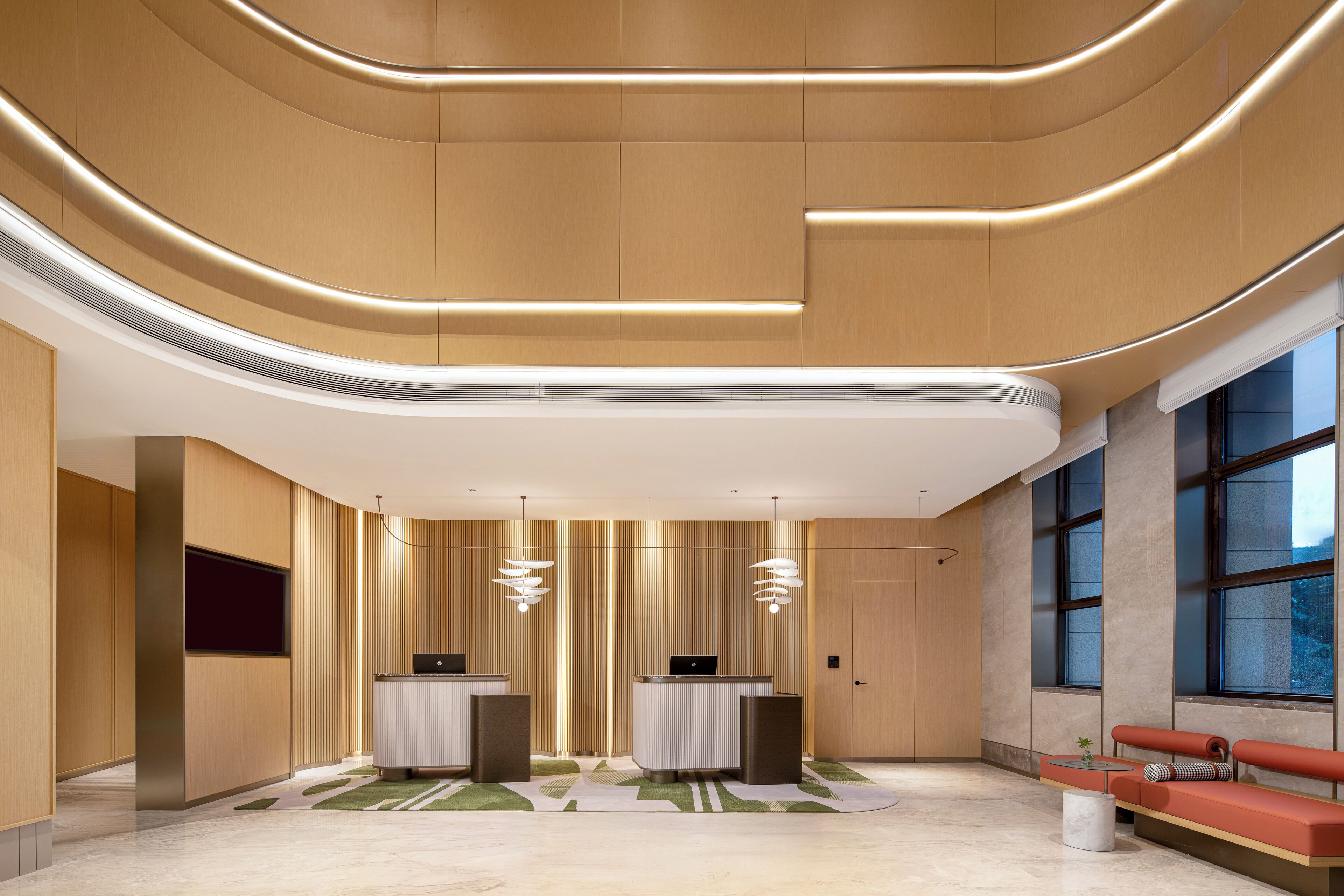 A modern reception area with curved ceiling lines, two reception desks, a seating area with a red sofa, and large windows providing natural light.