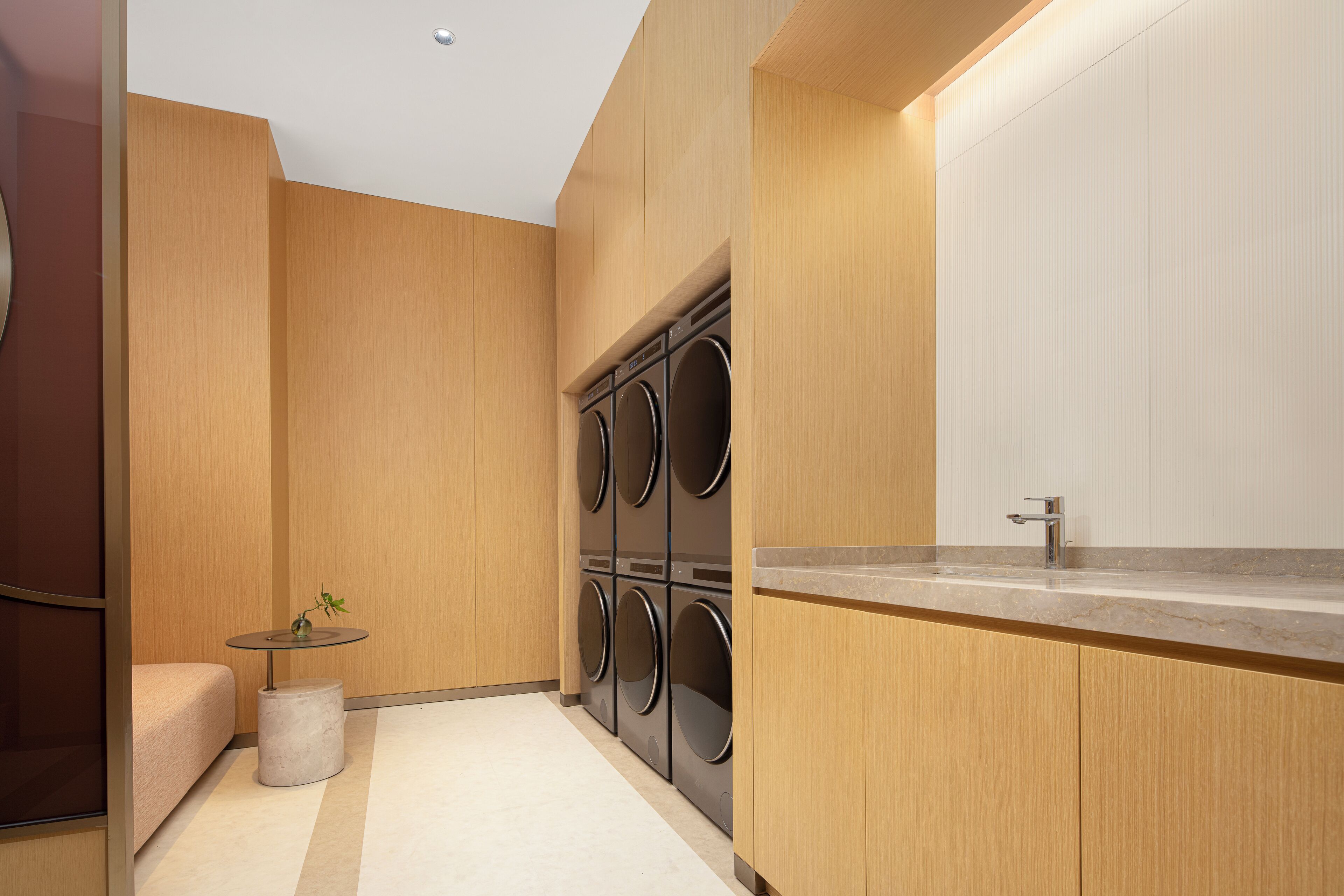A modern laundry room with a built-in washer and dryer, a small round table with a plant, and a bench.