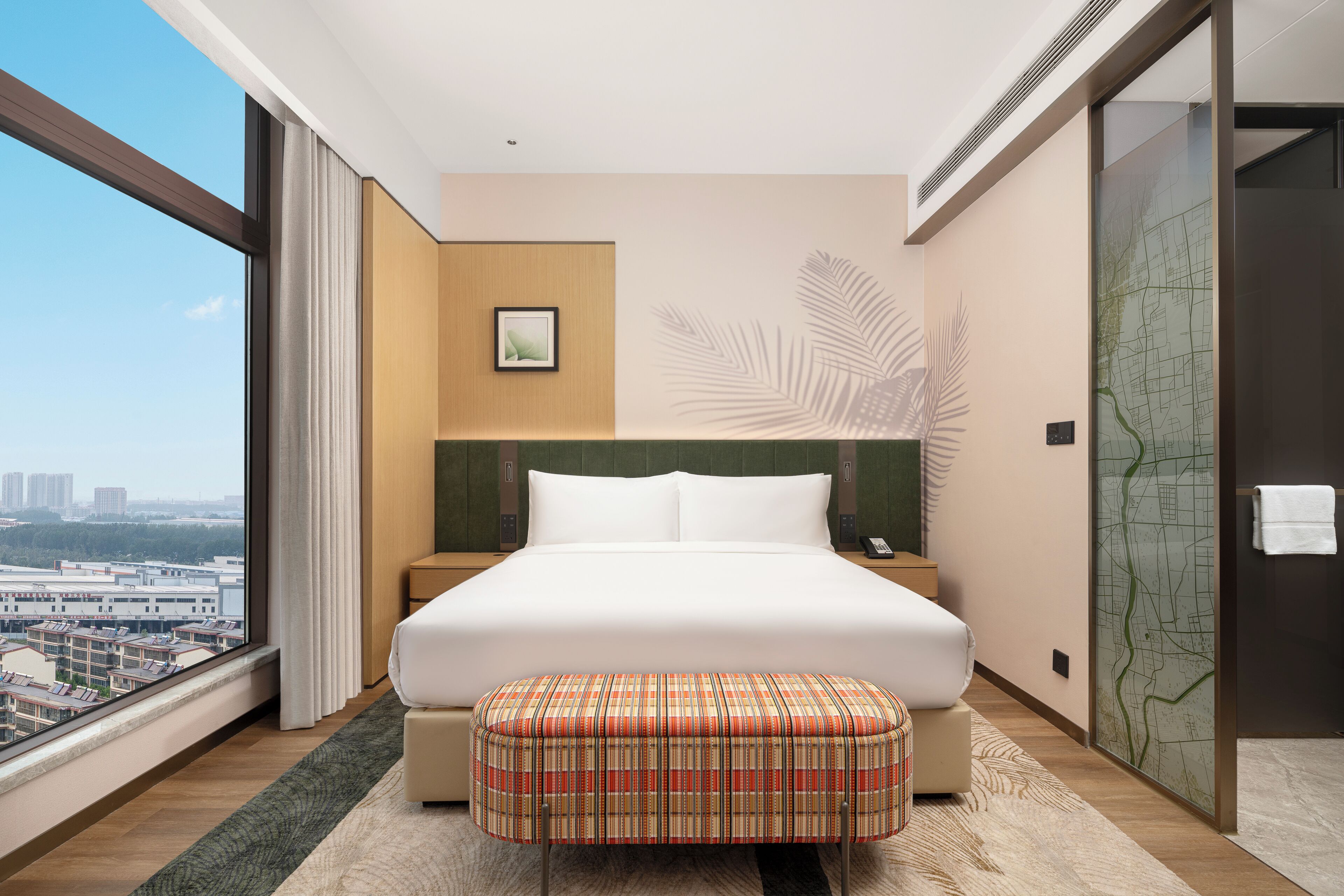 Ein Hotelzimmer mit einem großen Bett, Blick auf die Stadt, einer Karte an der Wand und einem Vorhangfenster.