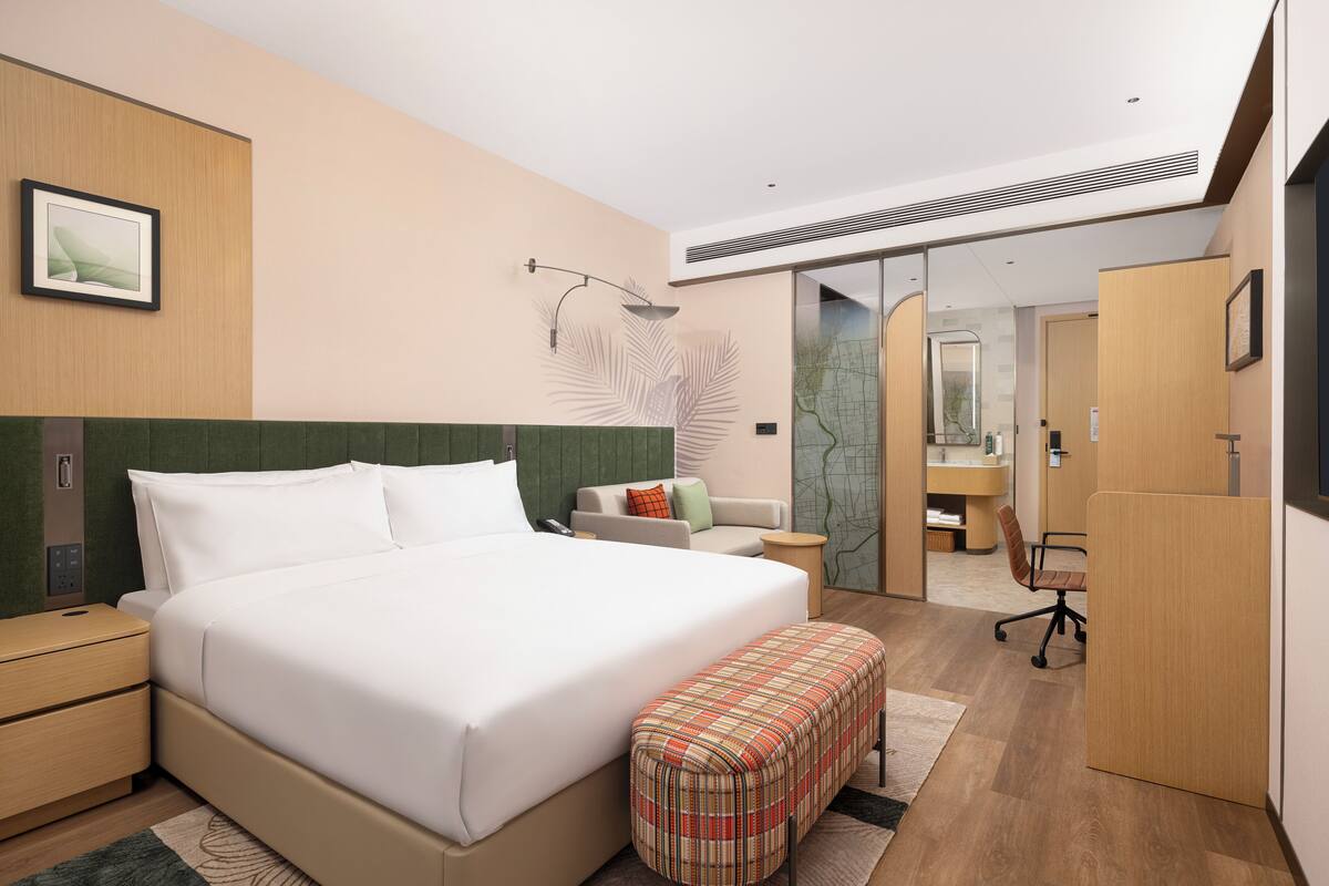 A modern hotel room with a large bed, a desk, and a seating area.