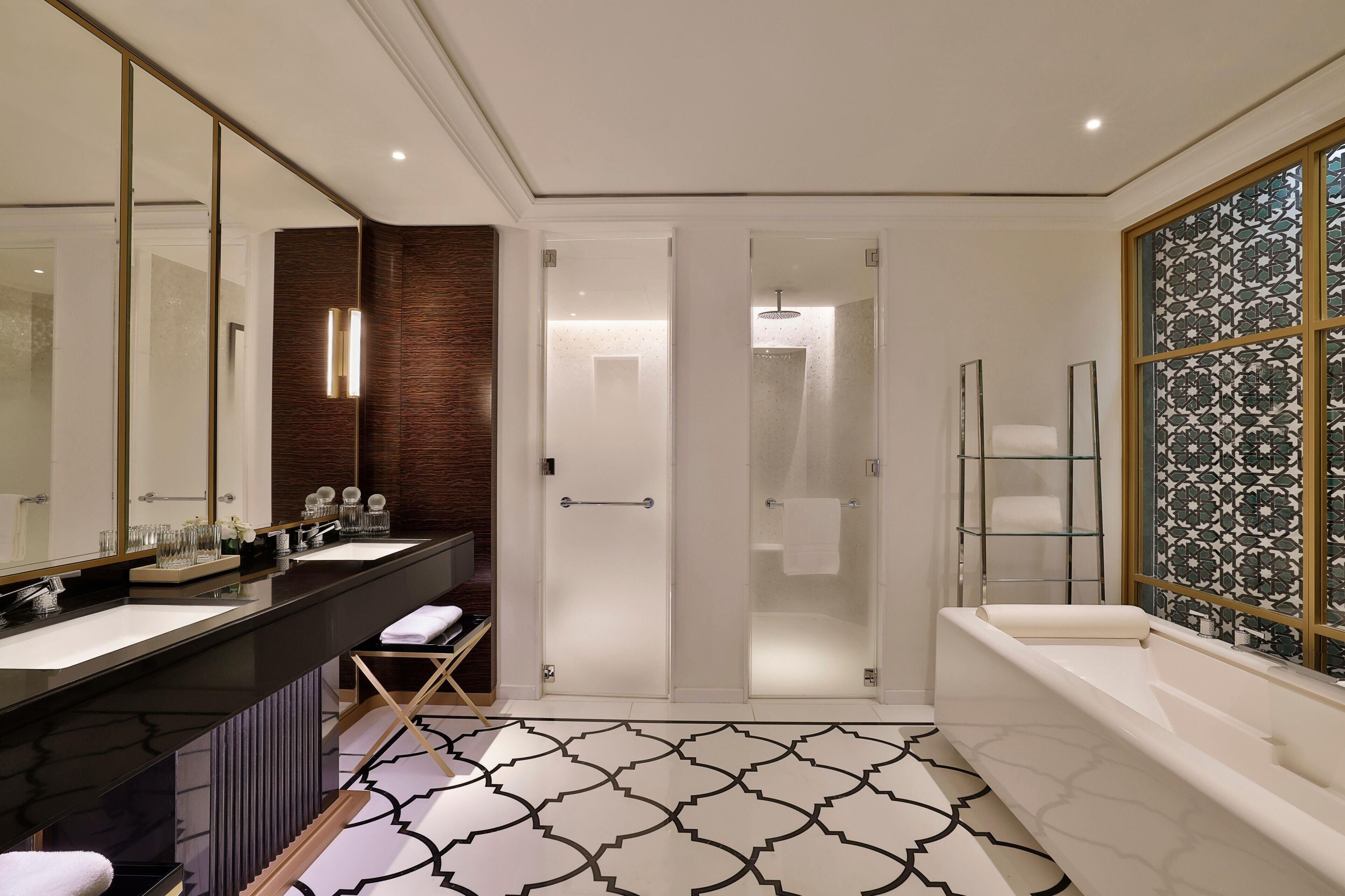 A modern bathroom with a dual sink vanity, a glass-enclosed shower, and a large bathtub.
