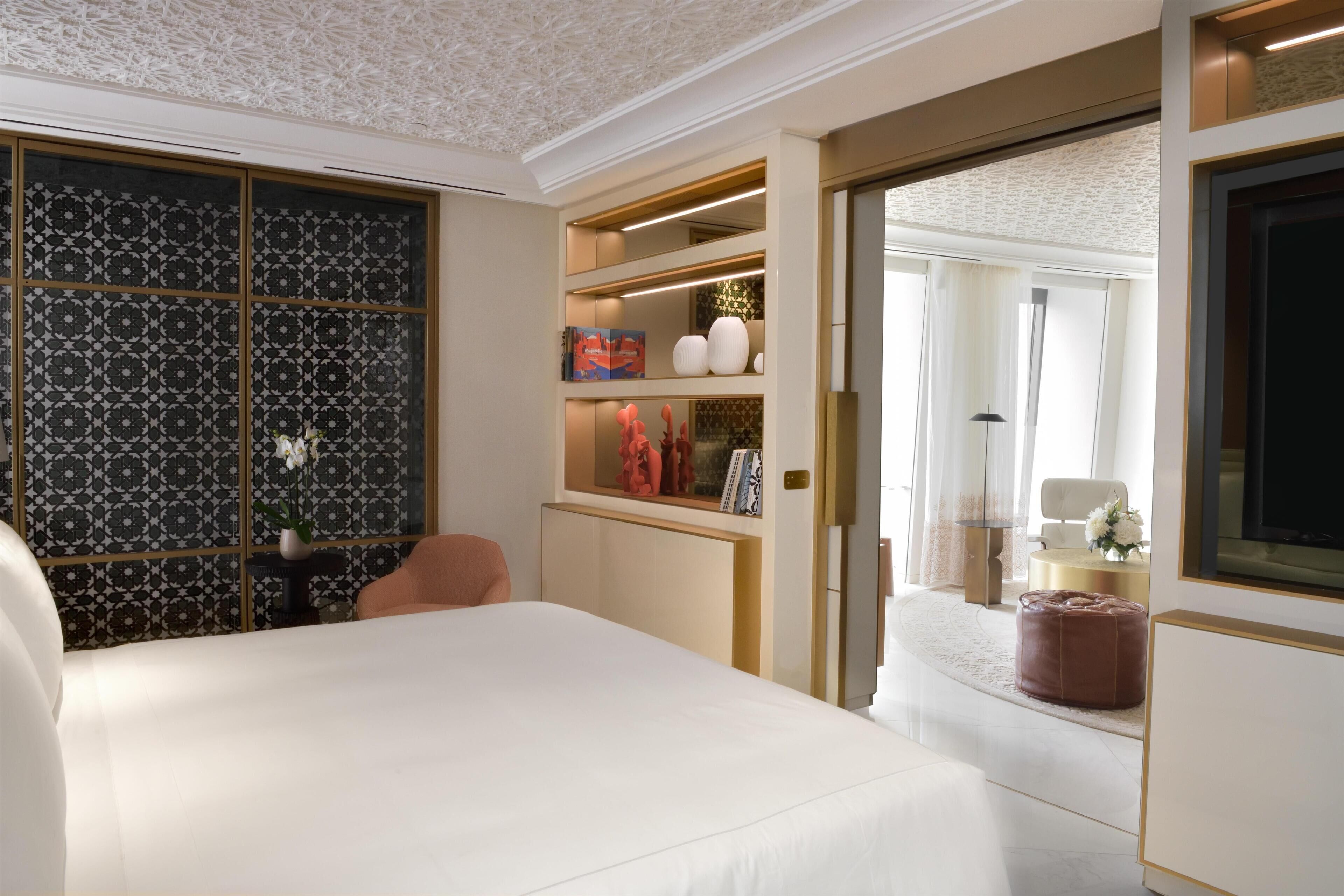 Una habitación de hotel moderna con una cama grande, un área de descanso con una silla, un tocador con espejo y un televisor.