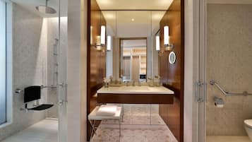 Un baño moderno con cabina de ducha de vidrio, tocador con espejo grande y inodoro con barra de apoyo.