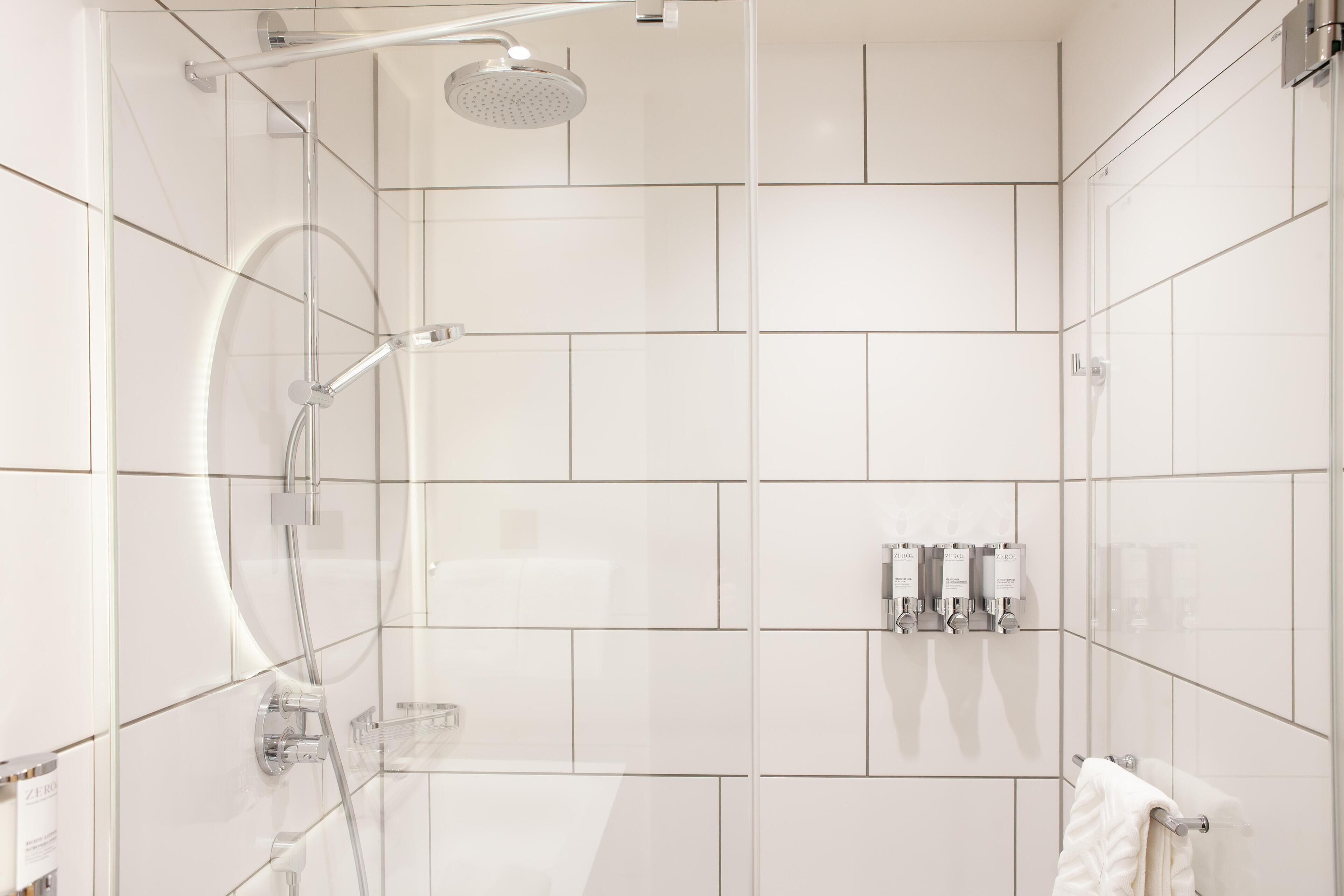 A modern bathroom with a glass-enclosed shower, white tiled walls, and a towel rack.