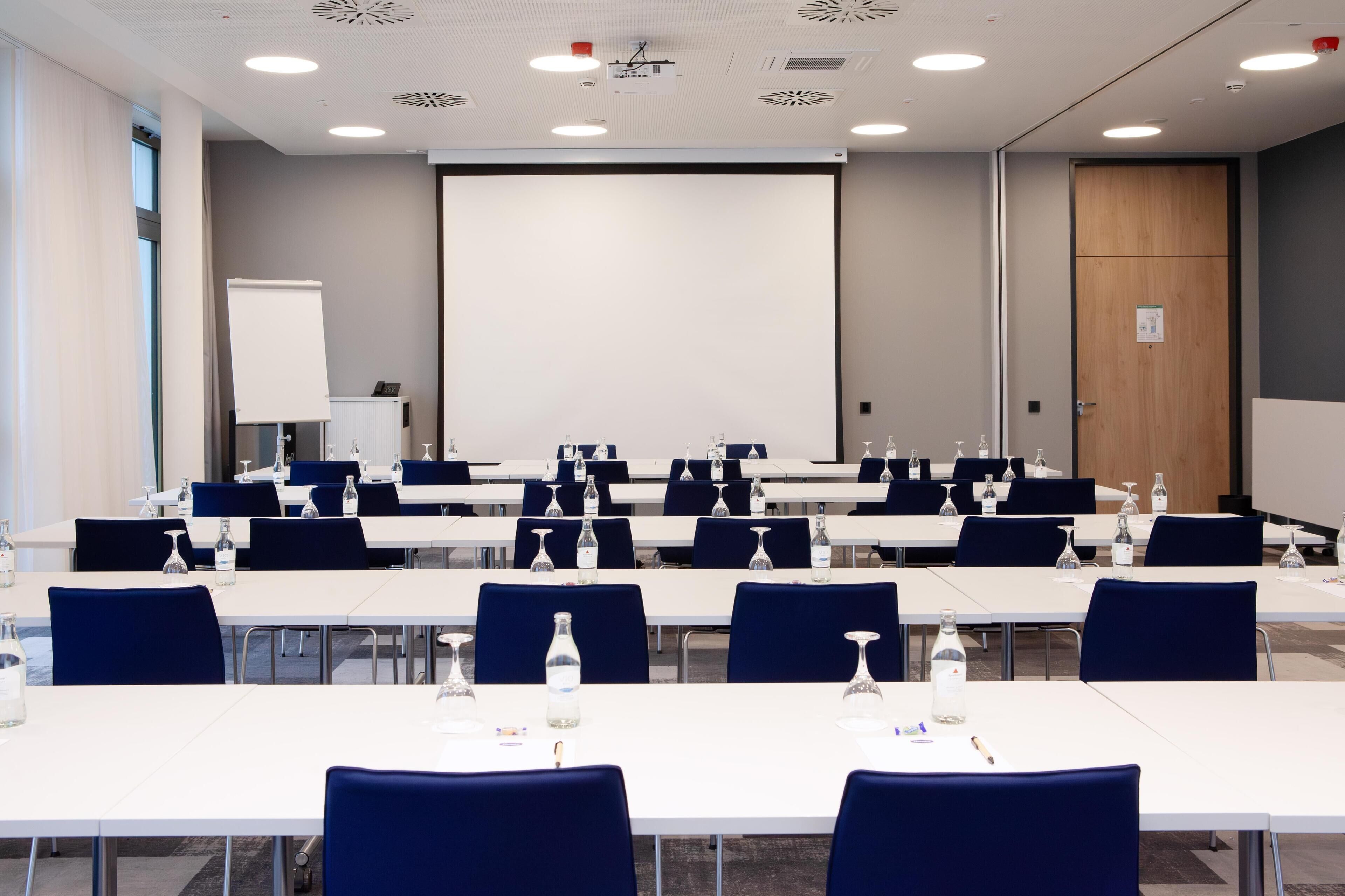 A conference room with multiple tables, chairs, and a large screen.