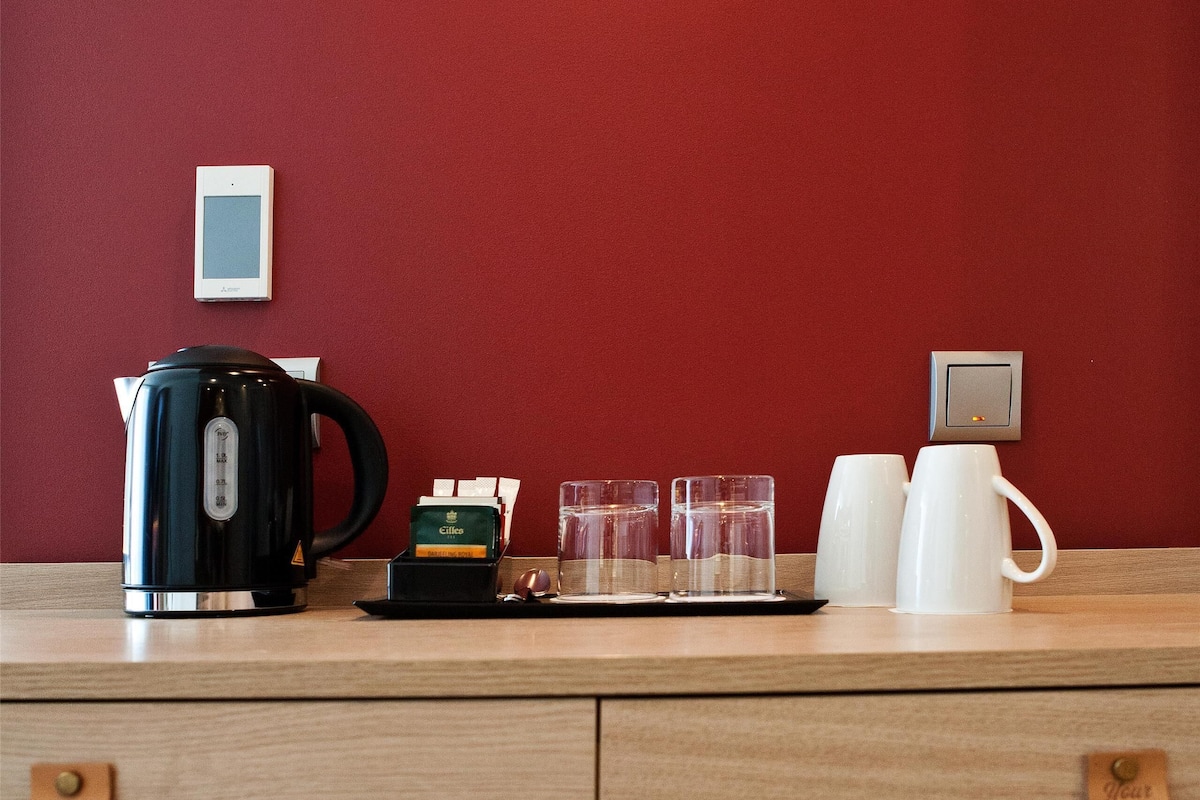 A wooden counter with a coffee maker, two white mugs, and a tray with coffee cups and a box of coffee pods.