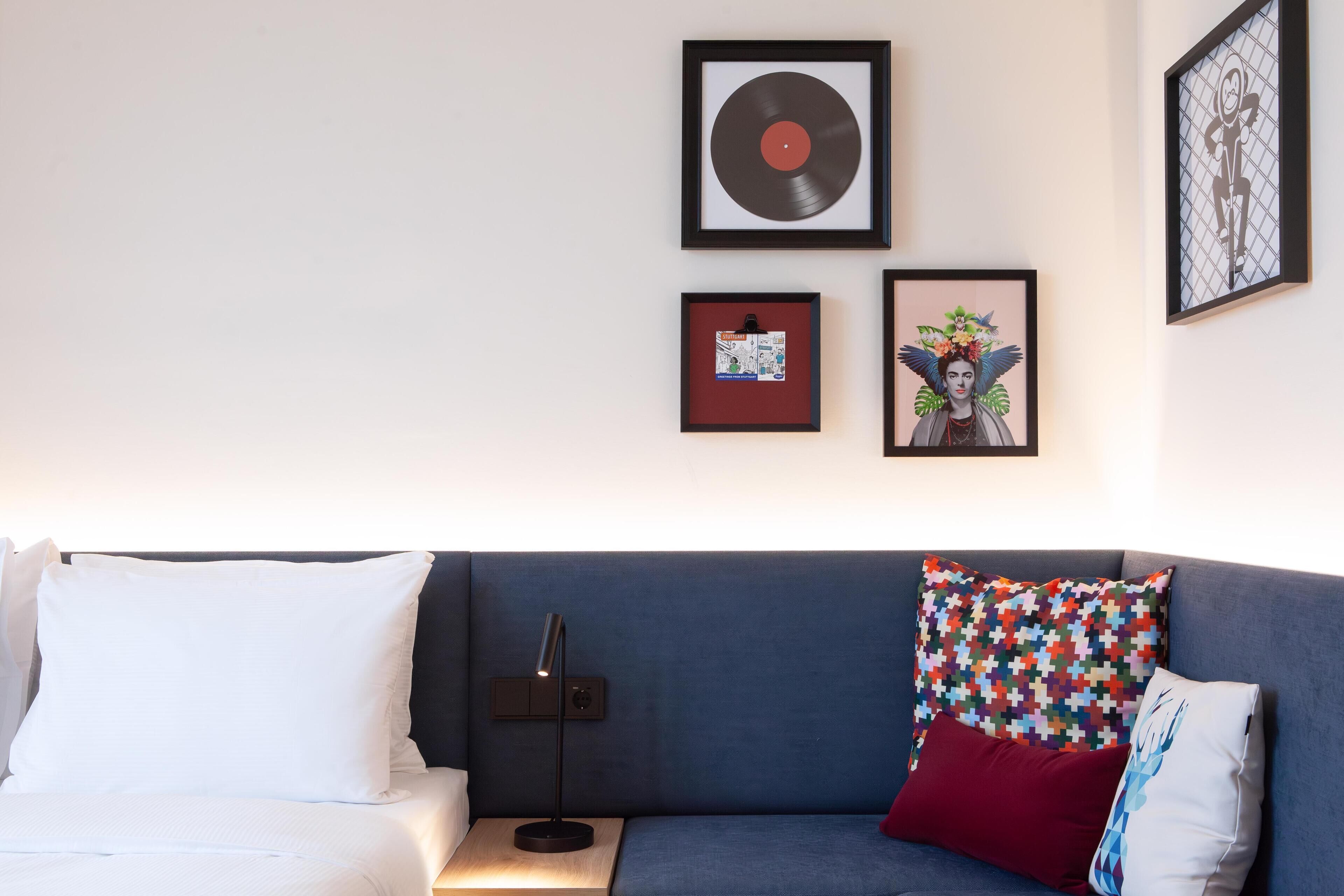 A modern living room with a blue sofa, white and red pillows, a black floor lamp, and framed artwork on the wall.