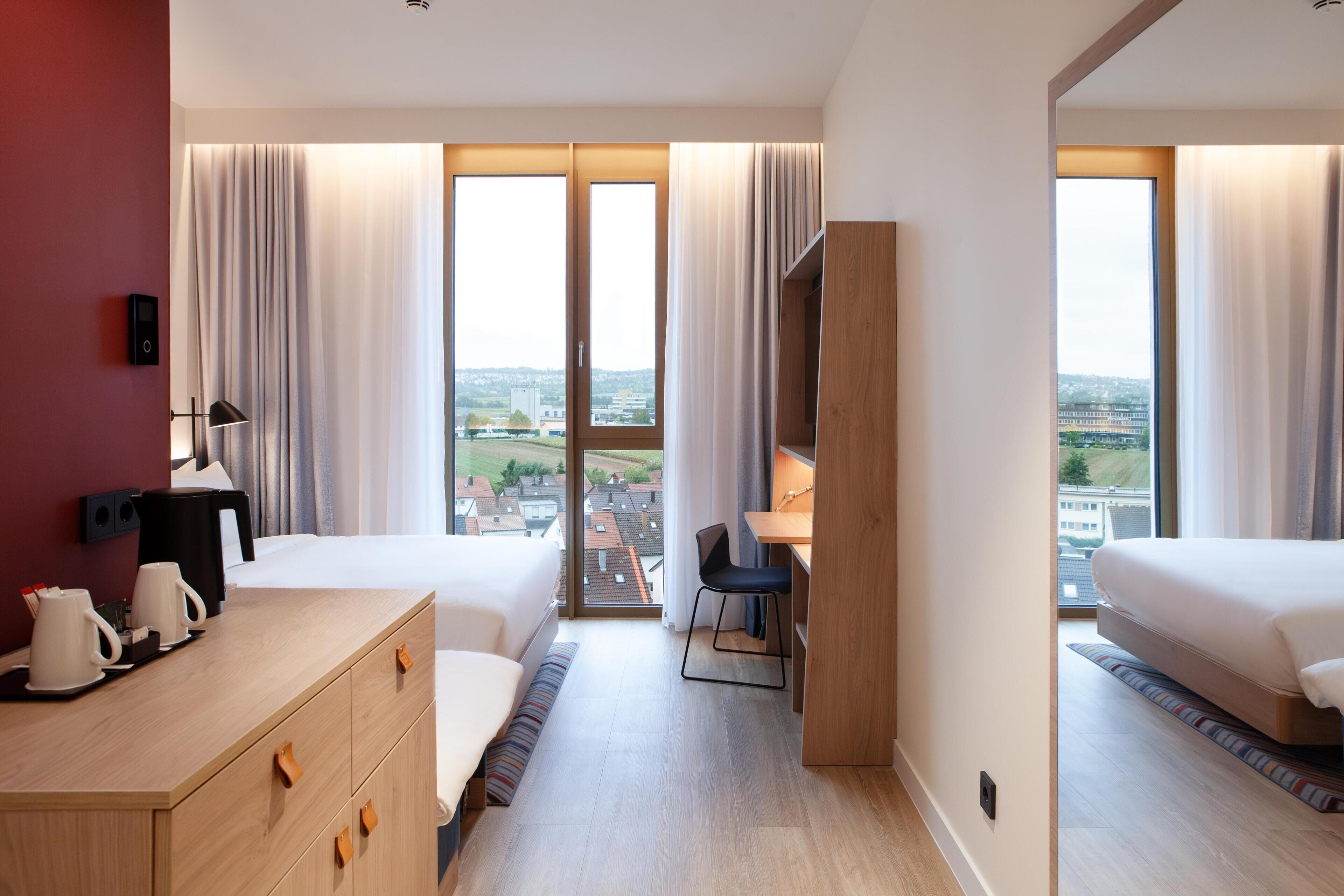 Une chambre d’hôtel avec deux lits, un bureau, une chaise, une machine à café et une vue sur la ville.