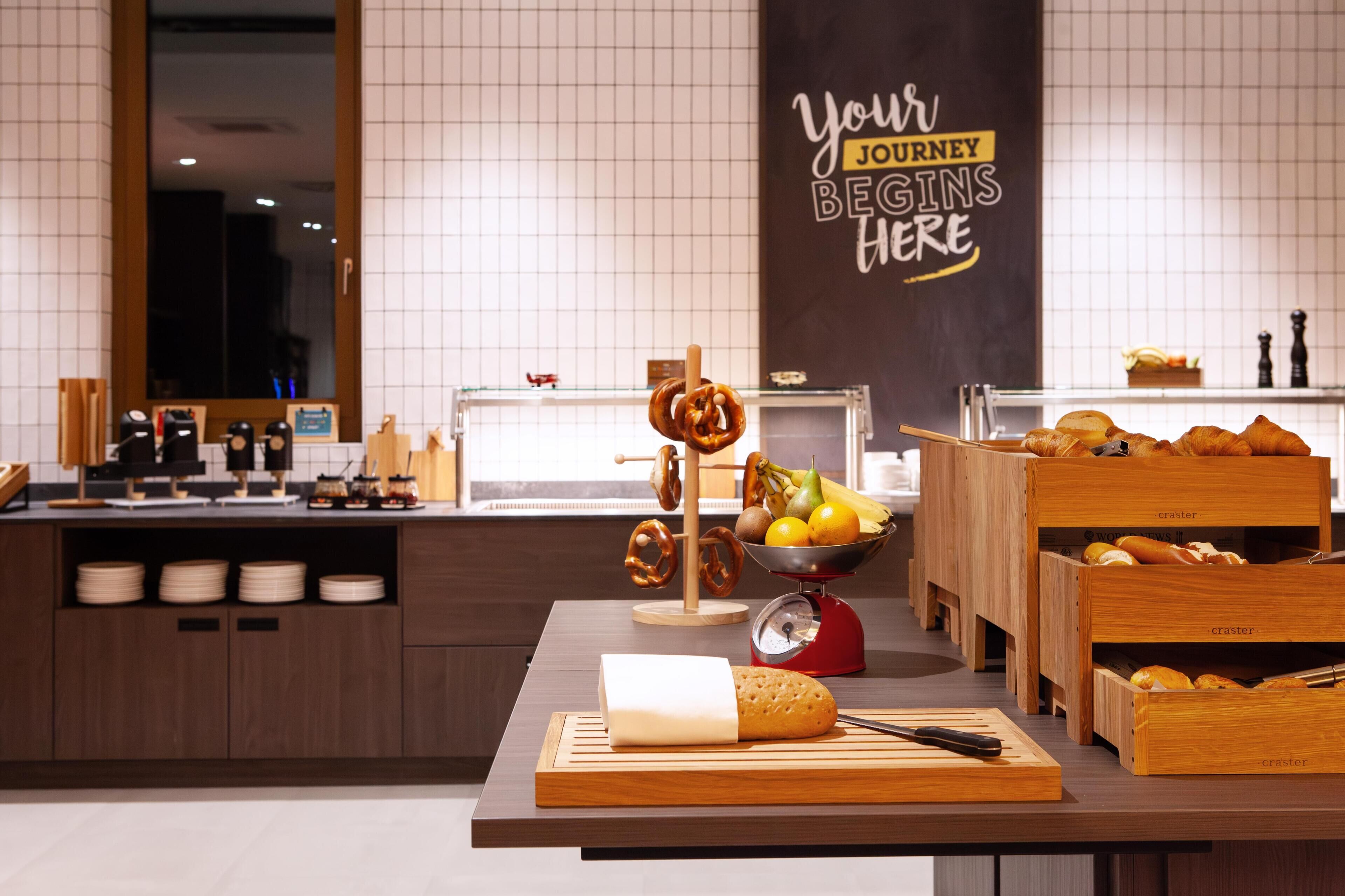 Ein Frühstücksbuffet mit verschiedenen Speisen und einem Schild mit der Aufschrift 'Ihre Reise beginnt hier'.