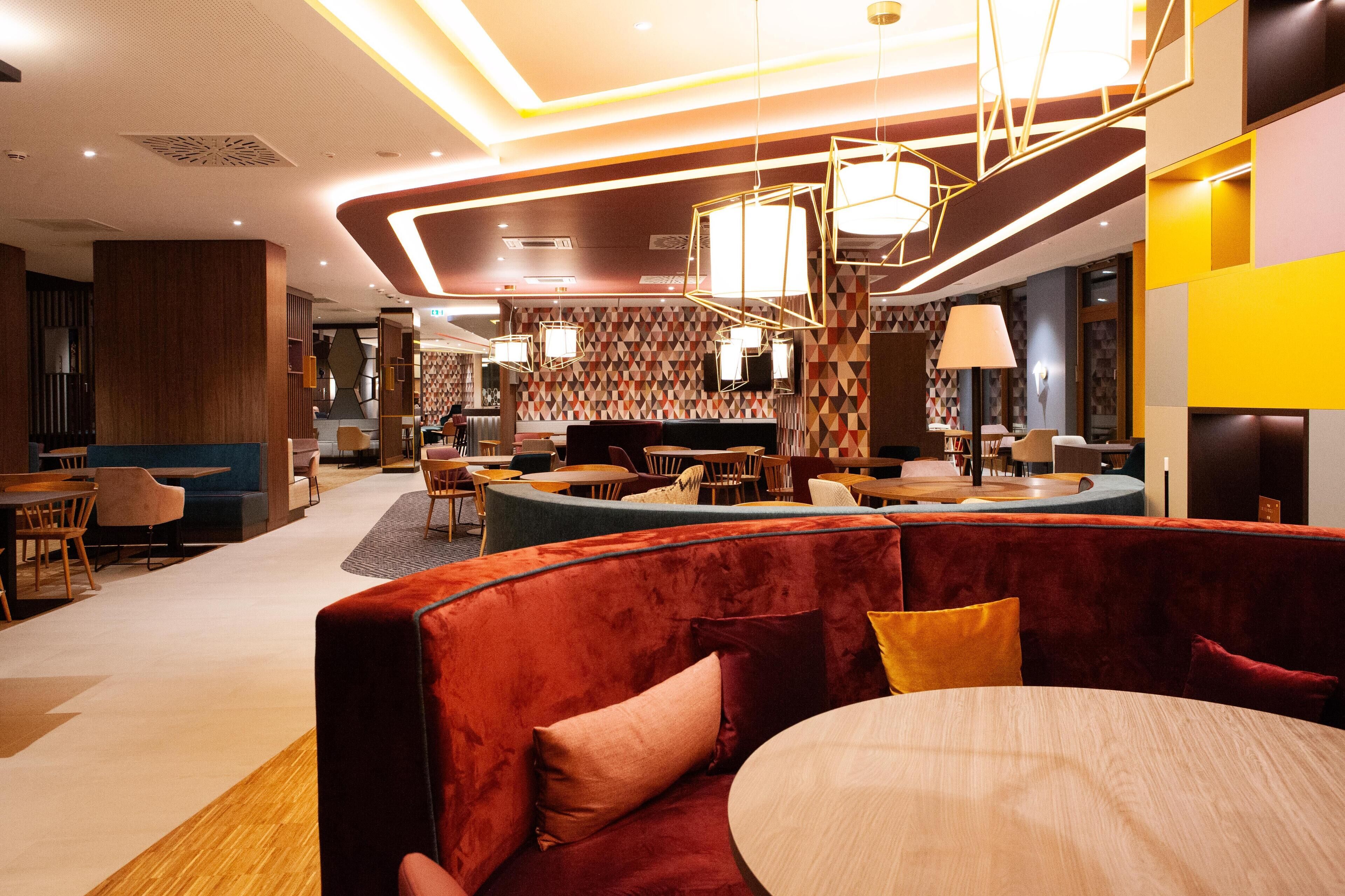A modern hotel lobby with a central seating area, a reception desk, and a patterned wall.