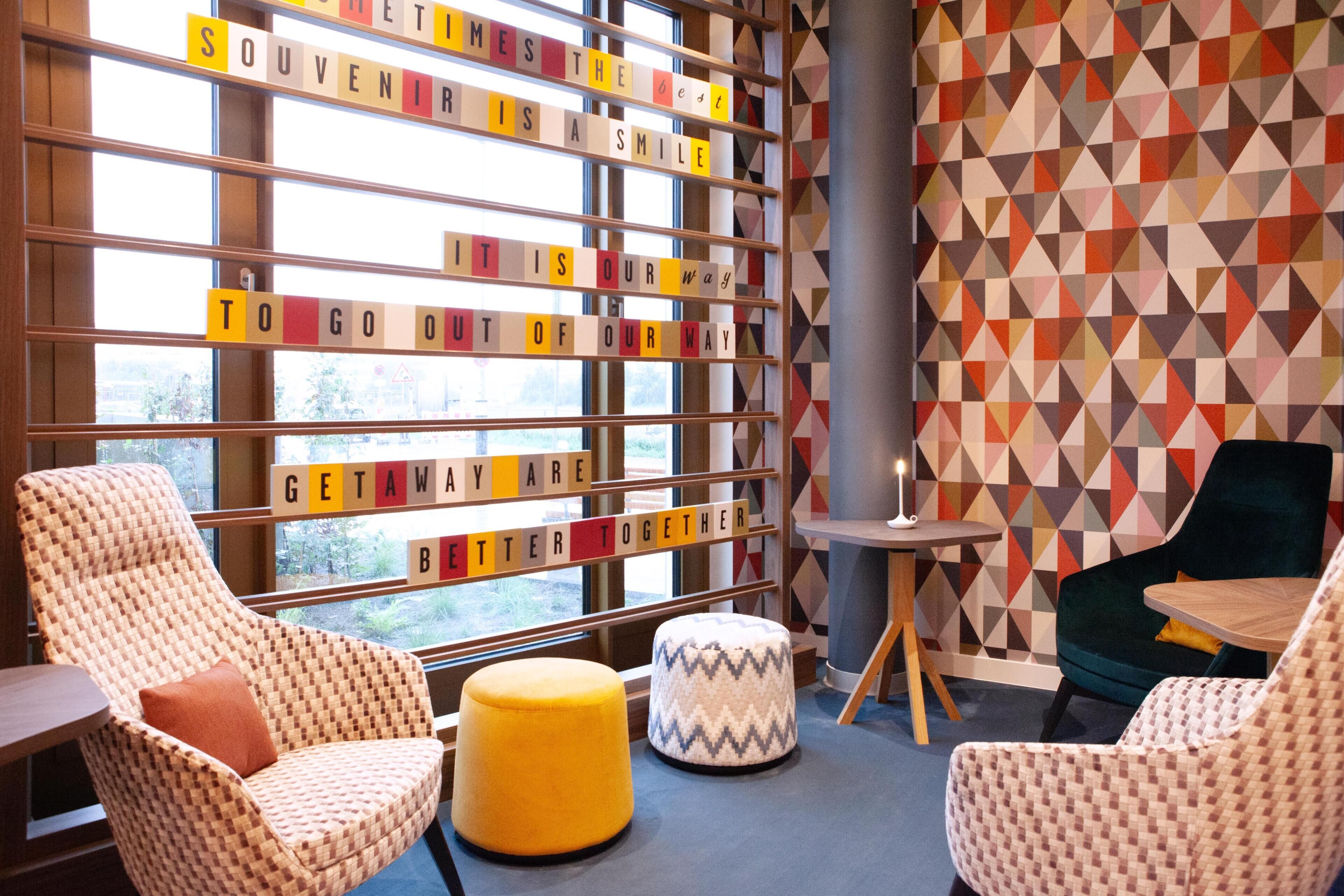 A cozy seating area with patterned chairs and ottomans, a small table, and a wall with geometric wallpaper.