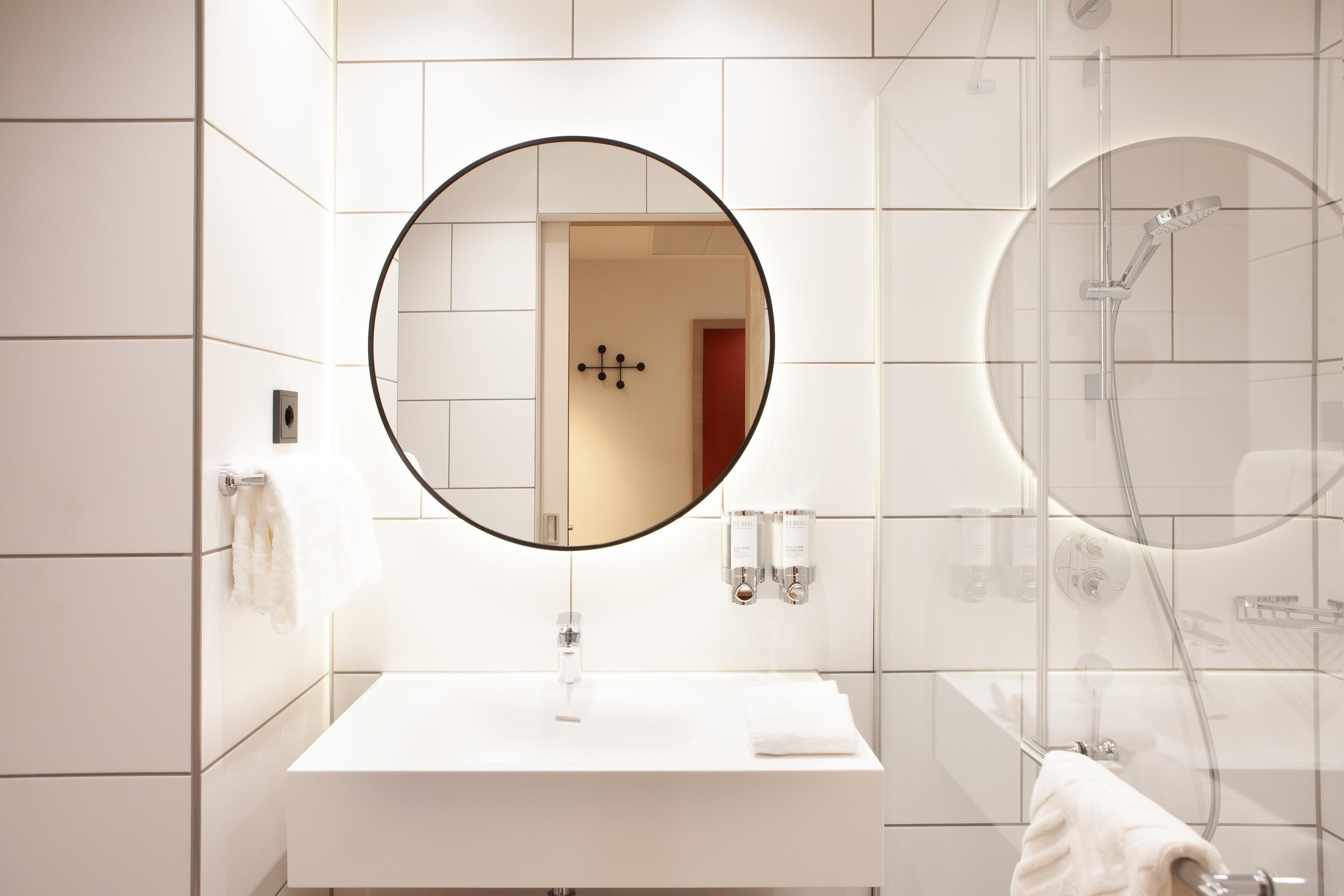 Een moderne badkamer met een witte wastafel, een ronde spiegel en een douche met glazen wanden.