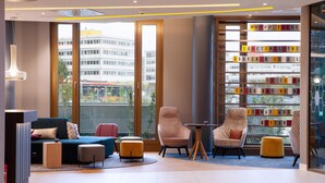 Una moderna hall d'albergo con un divano, poltrone, un tavolino e una libreria con lettere colorate.