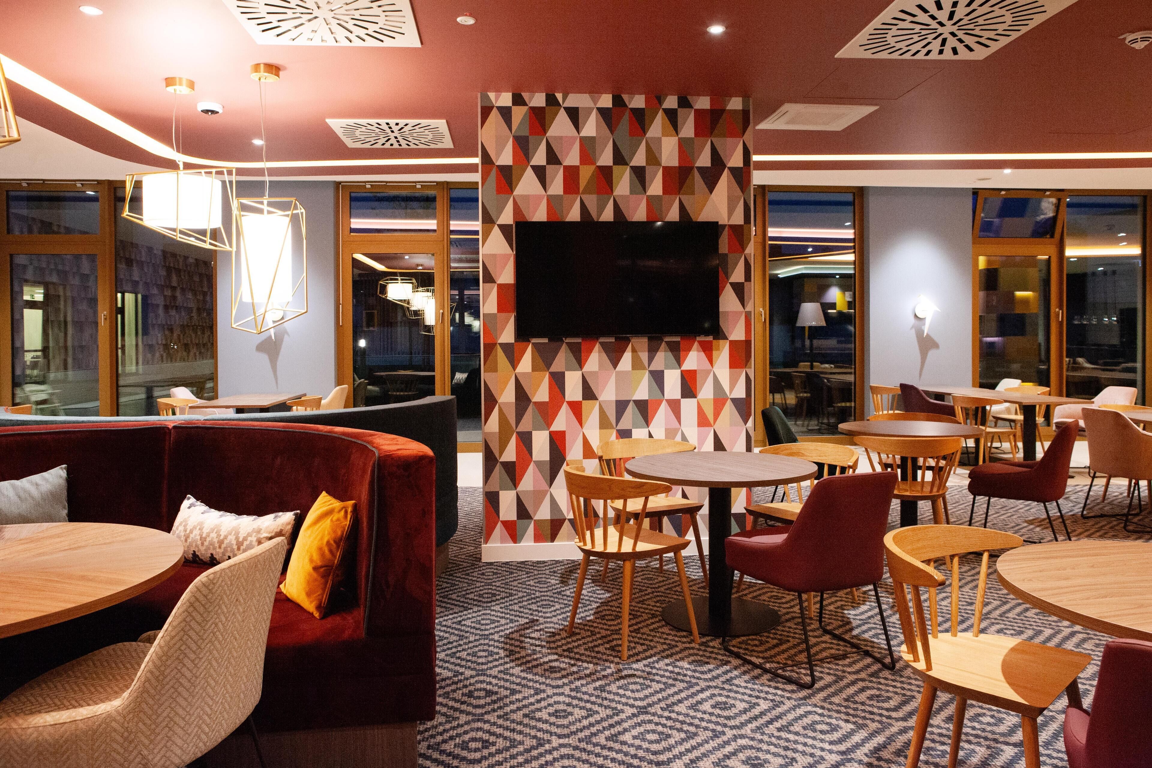 A modern lounge area with a geometric patterned wall, a flat-screen TV, and a mix of wooden and upholstered furniture.