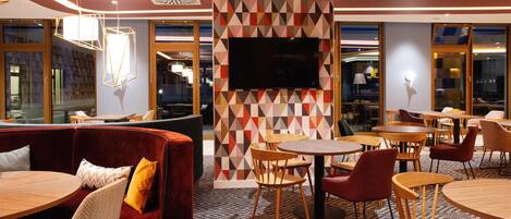 A modern lounge area with a geometric patterned wall, a flat-screen TV, and a mix of wooden and upholstered furniture.
