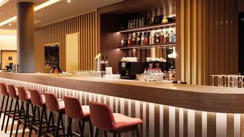 A bar area with a long counter, multiple stools, and shelves stocked with bottles and glasses.