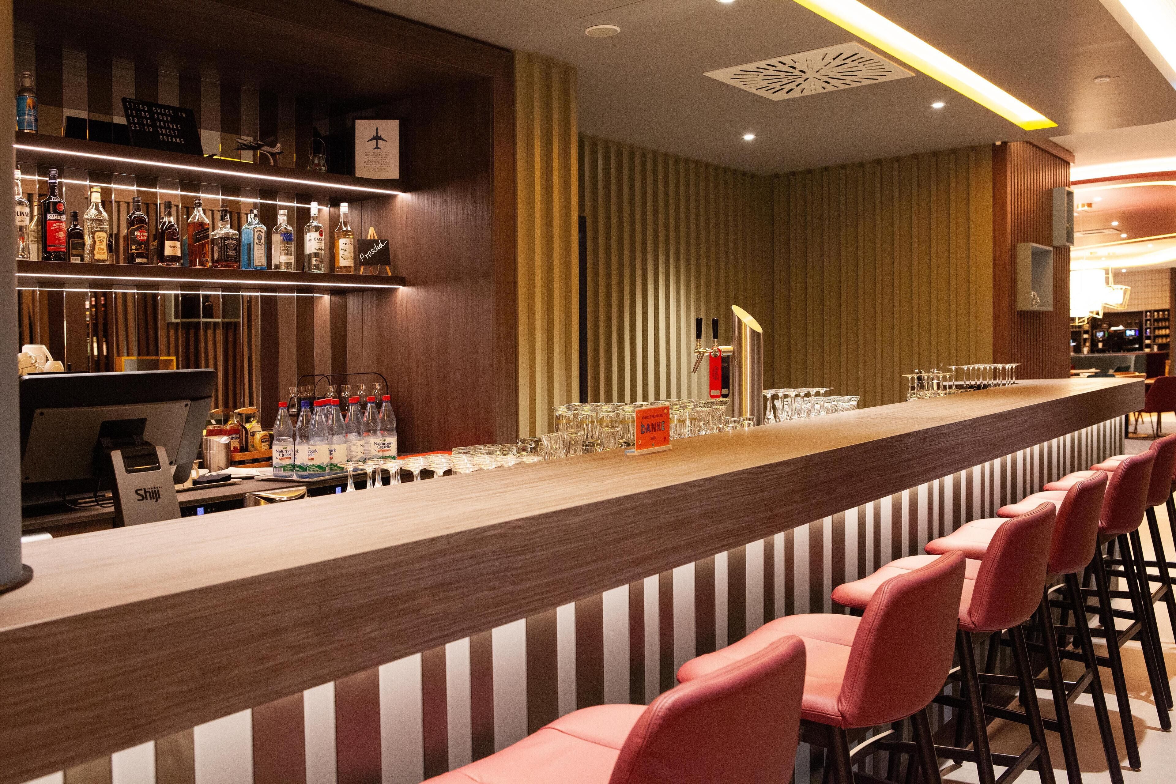A bar area with a long counter, multiple bottles of alcohol, glasses, and a cash register.