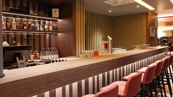 A bar area with a long counter, multiple bottles of alcohol, glasses, and a cash register.