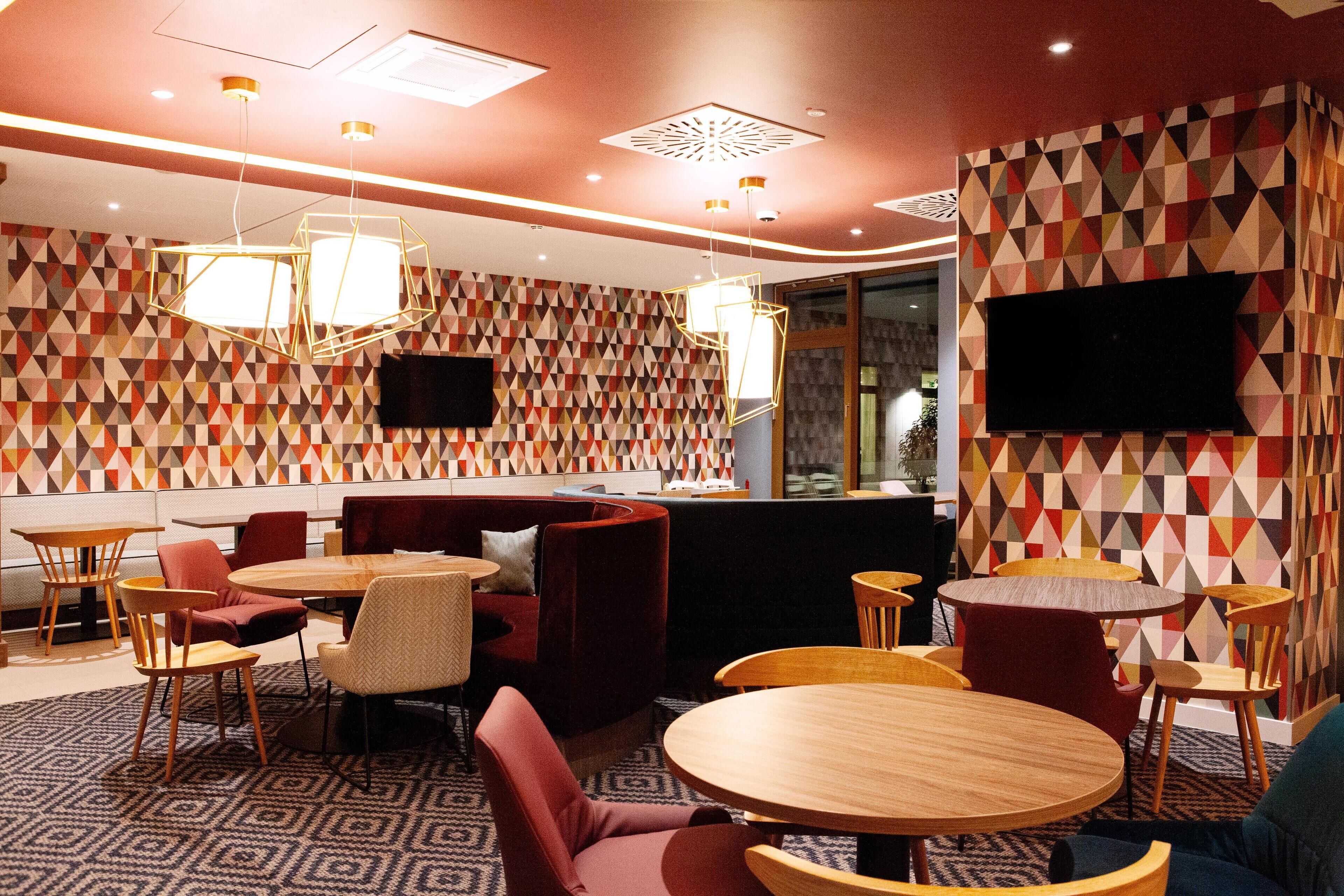 Un restaurant moderne avec des murs aux motifs géométriques, des tables rondes en bois et des sièges rembourrés de couleur rouge.