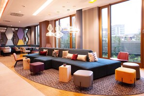 A modern hotel lobby with a large sectional sofa, ottomans, and a patterned rug. - Hampton By Hilton Stuttgart Airport (Filderstadt)