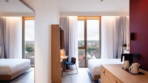Una camera d'albergo moderna con due letti, una scrivania, un comò e vista sulla città.