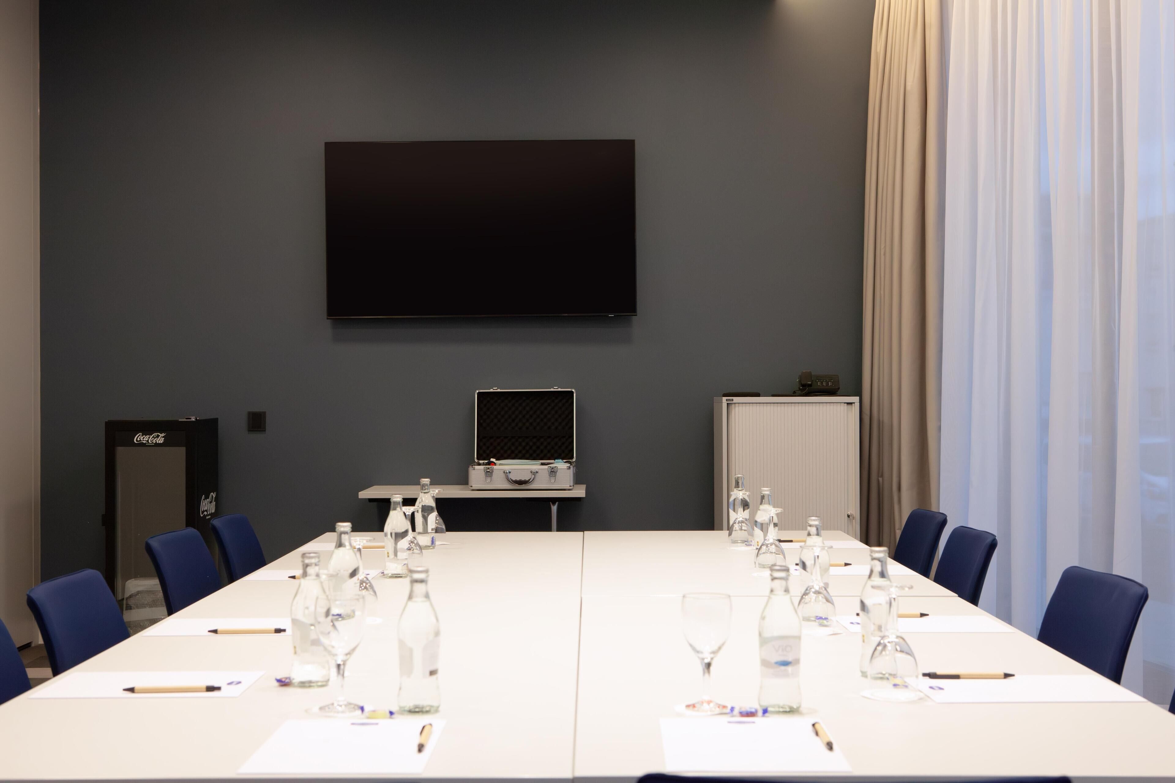 A conference room with a long table, chairs, a flat-screen TV, a projector, and a whiteboard.