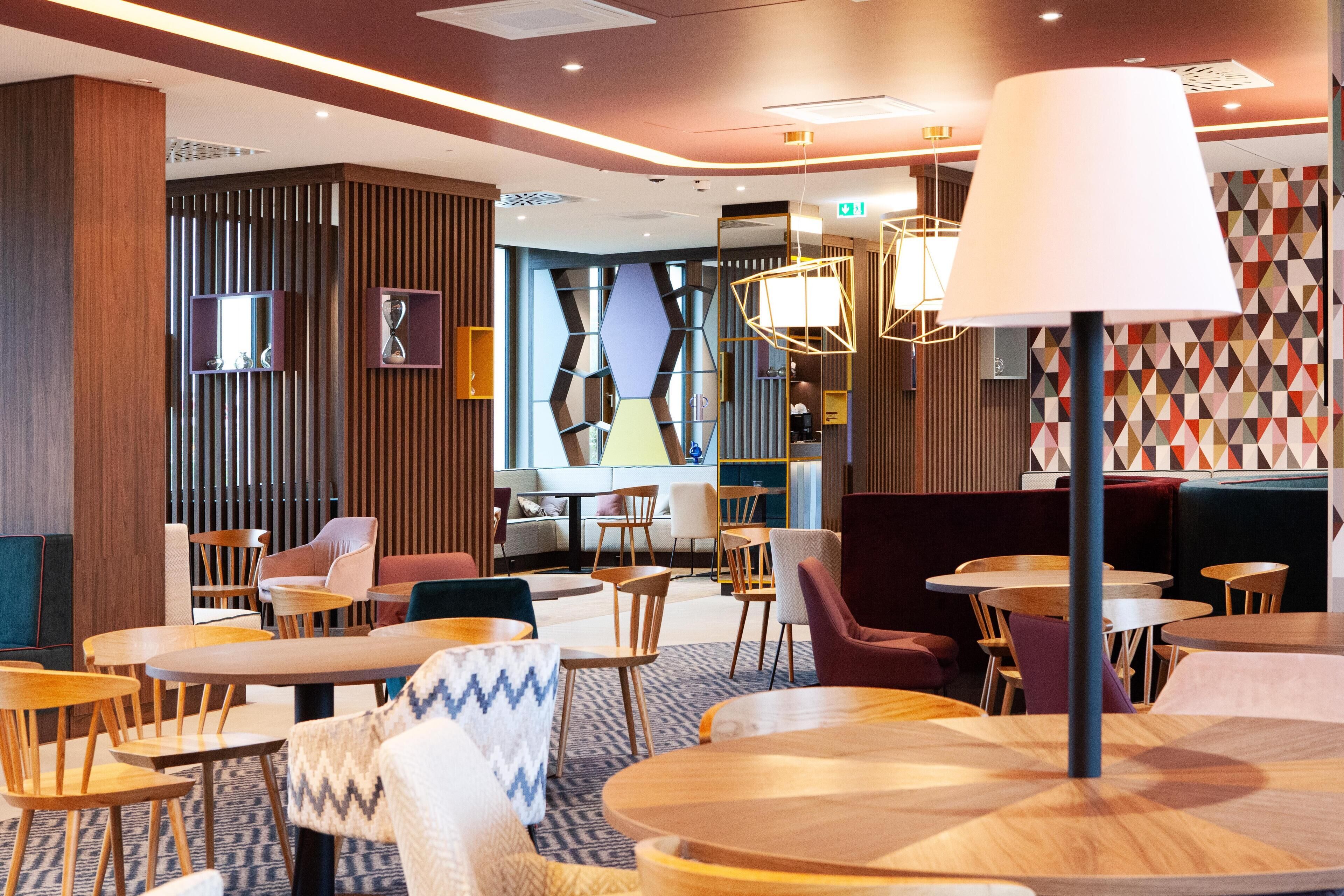 A modern hotel lobby with wooden furniture, a large lamp, and geometric wall patterns.