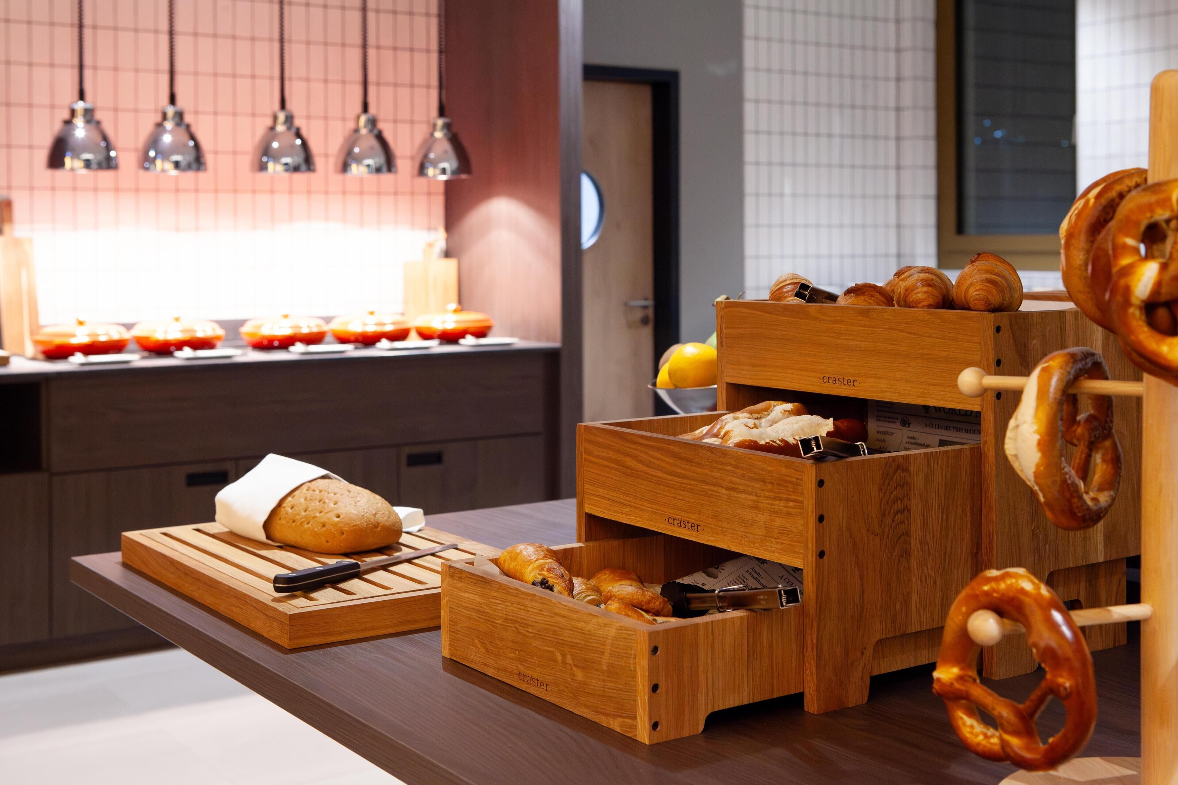 A kitchen counter with wooden bread boxes, a cutting board with a loaf of bread, and a hanging pretzel rack.