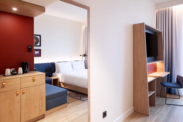 A modern hotel room with a bed, a desk with a chair, a wardrobe, and a TV. - Hampton By Hilton Stuttgart Airport (Filderstadt)