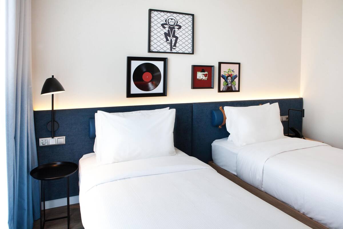 A hotel room with two beds, a nightstand, and a lamp.