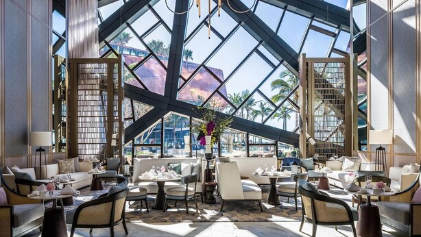 A spacious, well-lit lounge area with comfortable seating and a large glass window offering a view of palm trees and a building. - Luxe Absolute beachfront 2B River and Sunset views/Spa/Sauna/Steam/Free parking! (Surfers Paradise)