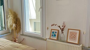 A bedroom with a bed, a radiator, a window with a blind, and wall decorations including framed pictures.