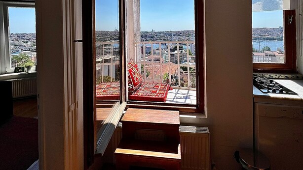 A room with a view of a cityscape through large windows, a wooden staircase, and a radiator.