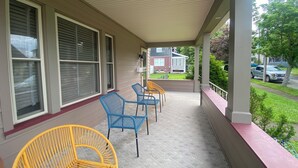 A covered porch with blue and yellow wicker chairs, a red railing, and a view of a residential street.