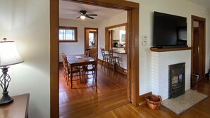 A dining area with a wooden table and chairs, a ceiling fan, and a fireplace with a TV above it.