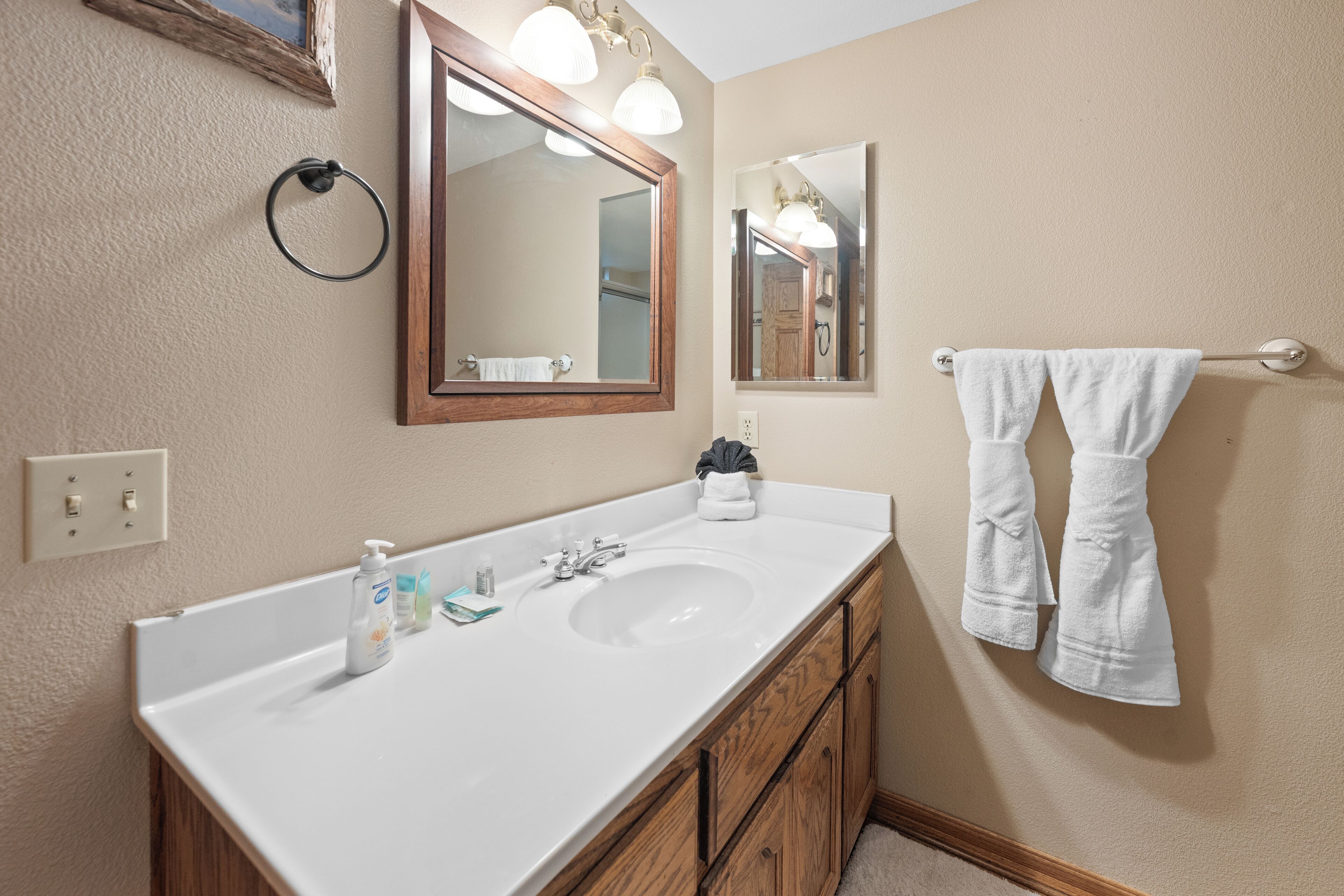 A bathroom with a white sink, wooden cabinets, two mirrors, and a towel rack with towels.