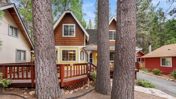 A cabin with a wooden deck, large trees, and a clear sky.