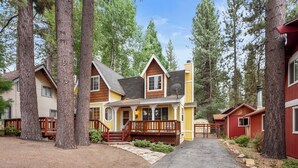 A two-story house with a front porch, surrounded by tall trees.